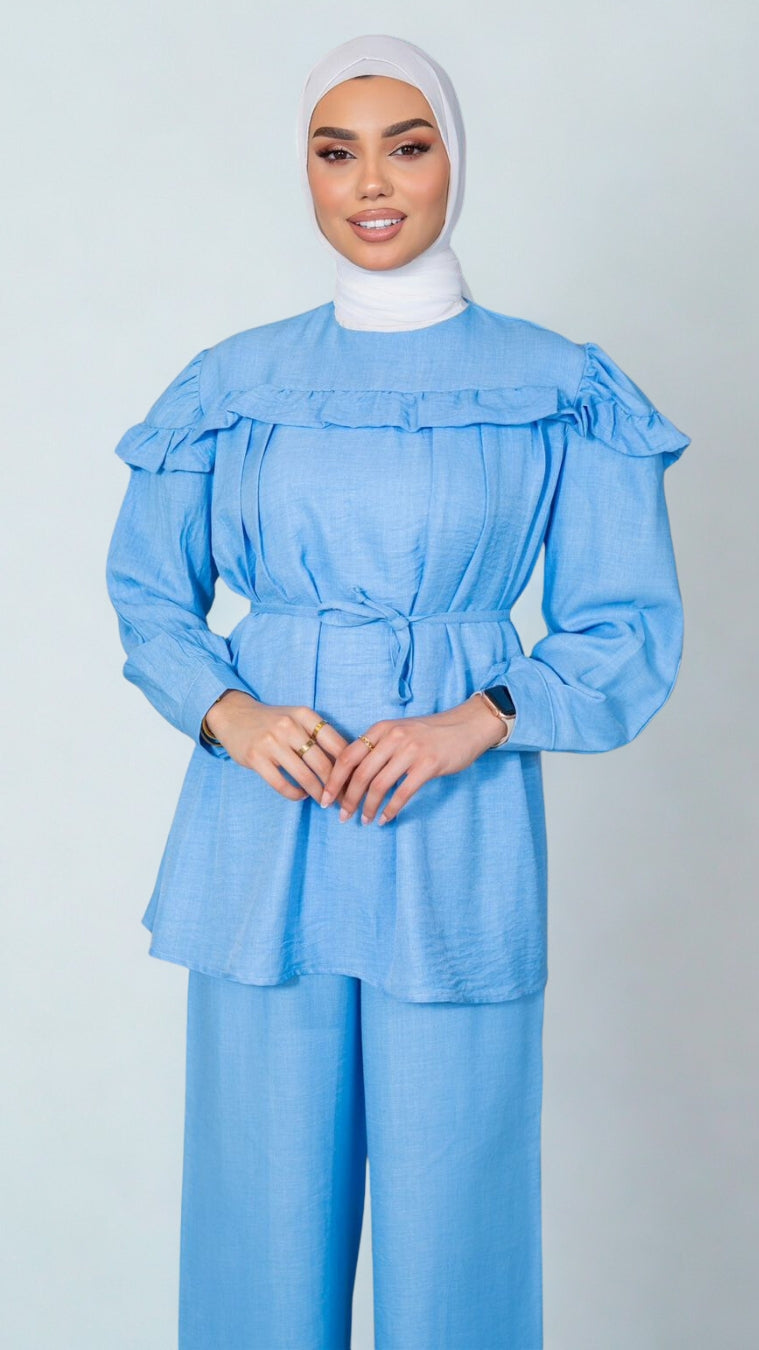 Woman wearing a light blue outfit with a matching hijab on a plain background