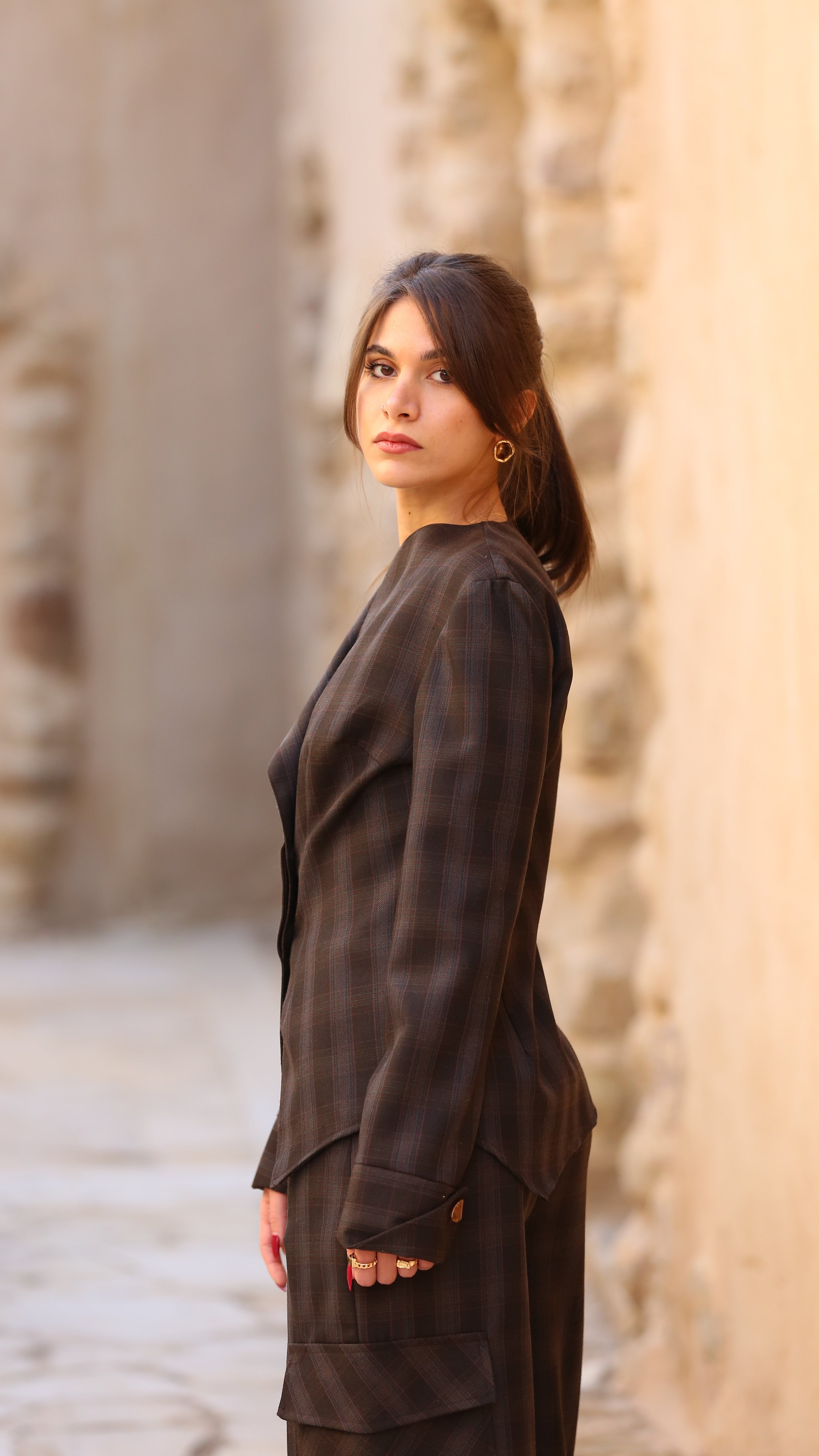Woman in a dark outfit standing in front of stone walls.