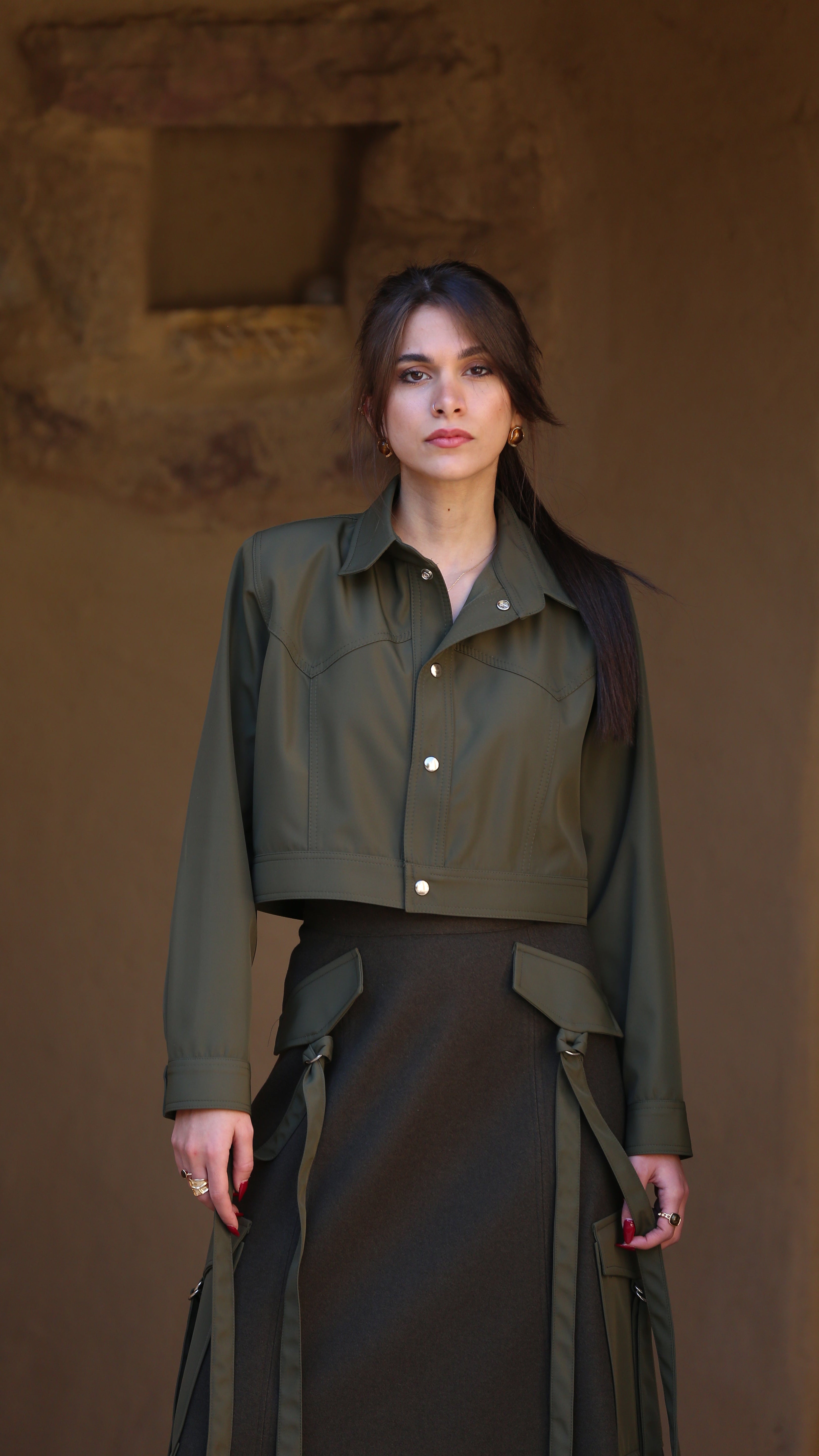 Woman wearing a green jacket and dark skirt against a brown background