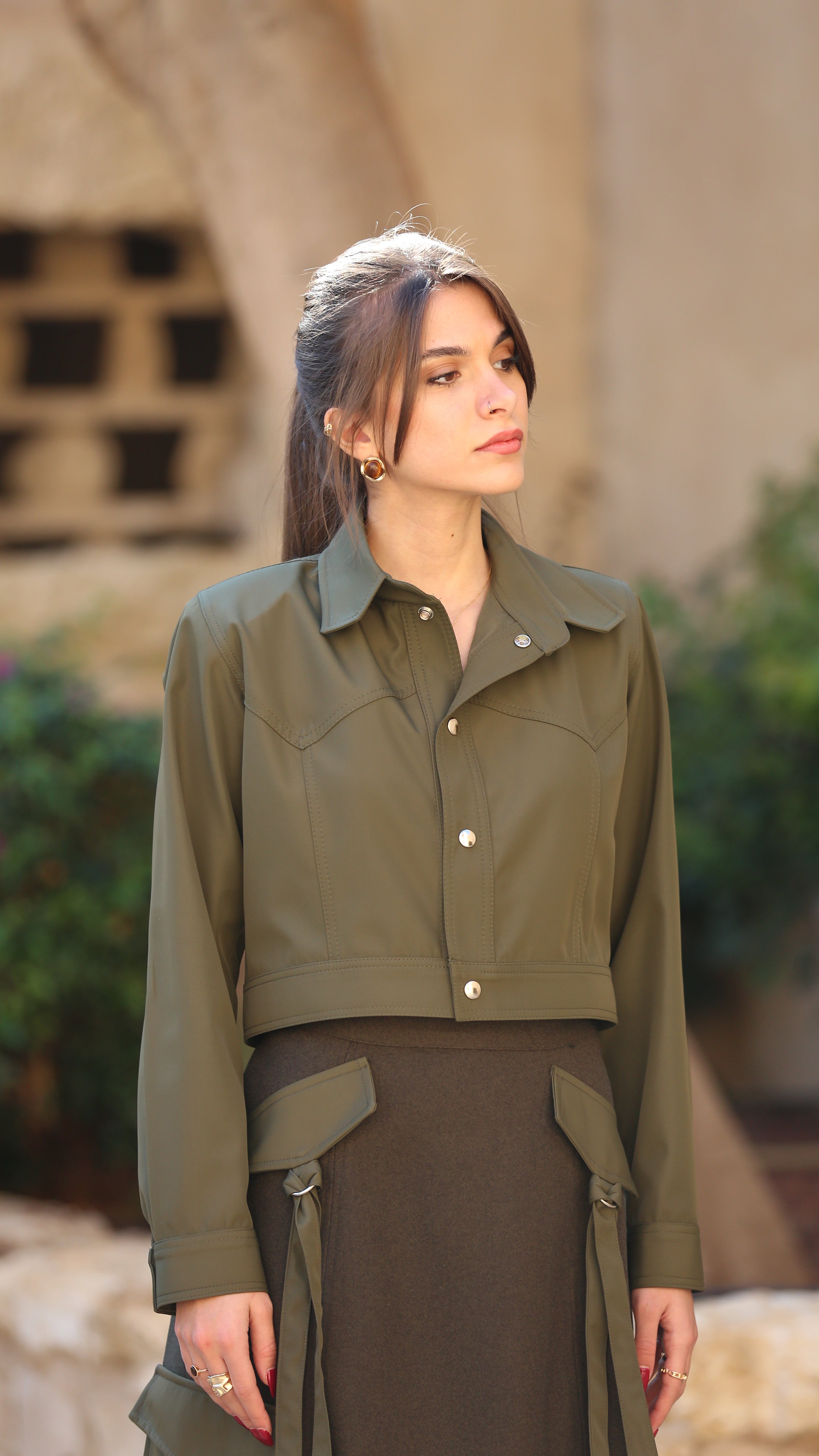 Woman wearing a green jacket and brown skirt standing outdoors with a blurred background
