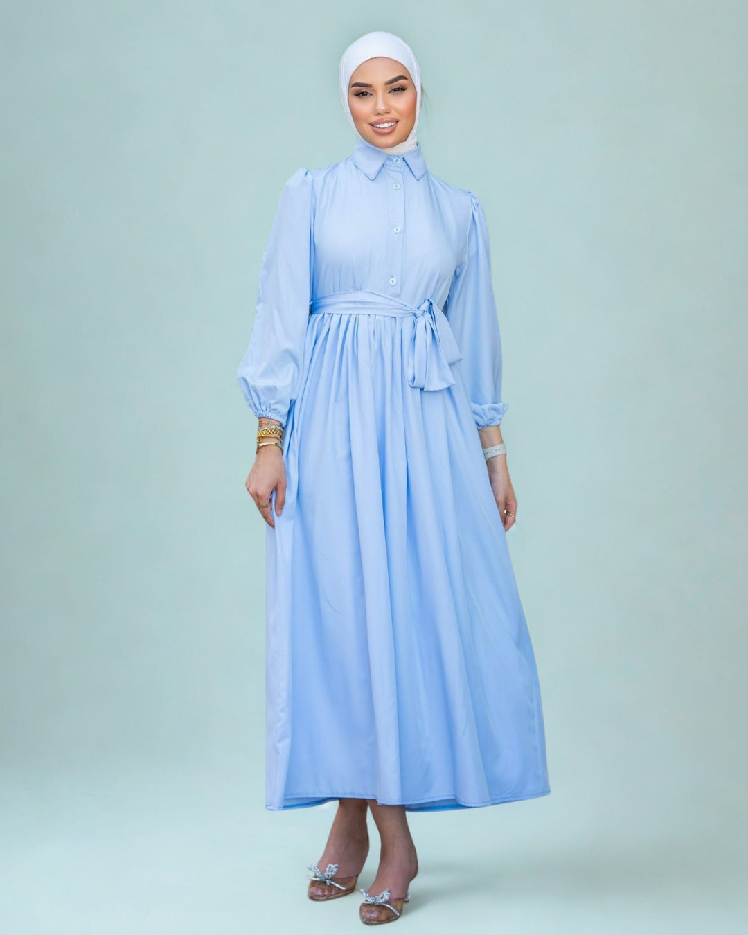 Woman wearing a light blue dress with a white headscarf on a light gray background