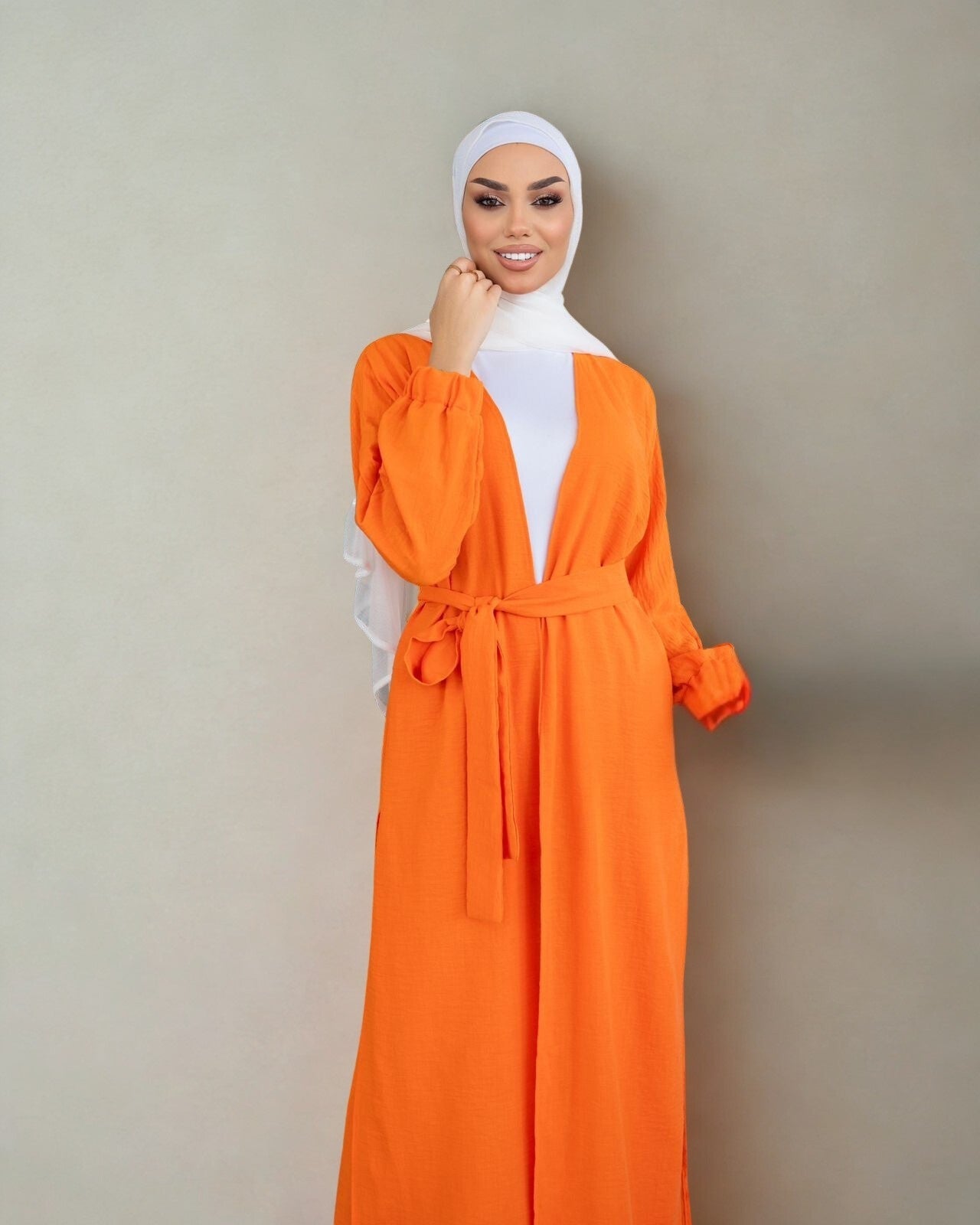 Woman wearing an orange dress with a white hijab against a beige background