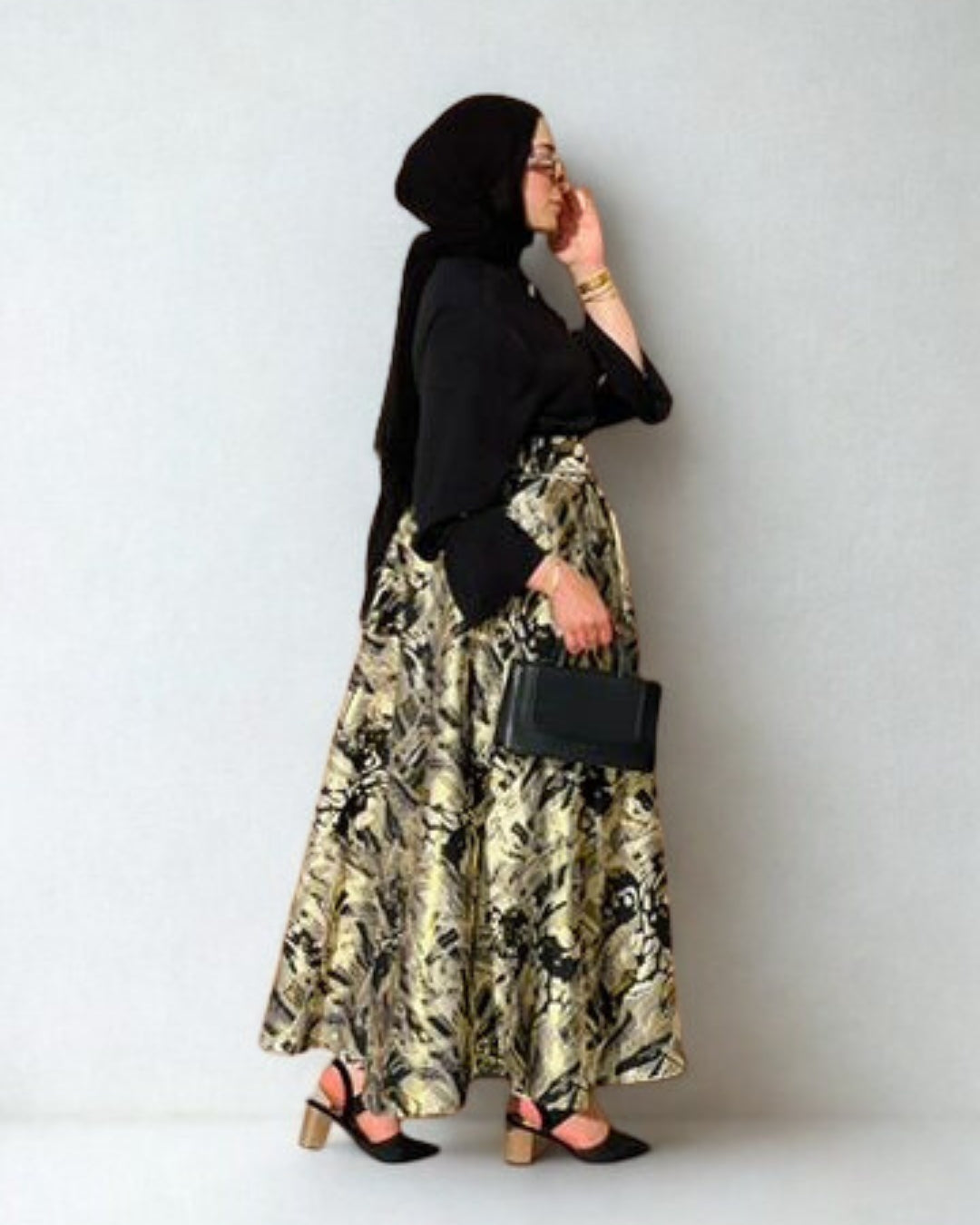 Woman wearing a black hijab and floral skirt with a plain background