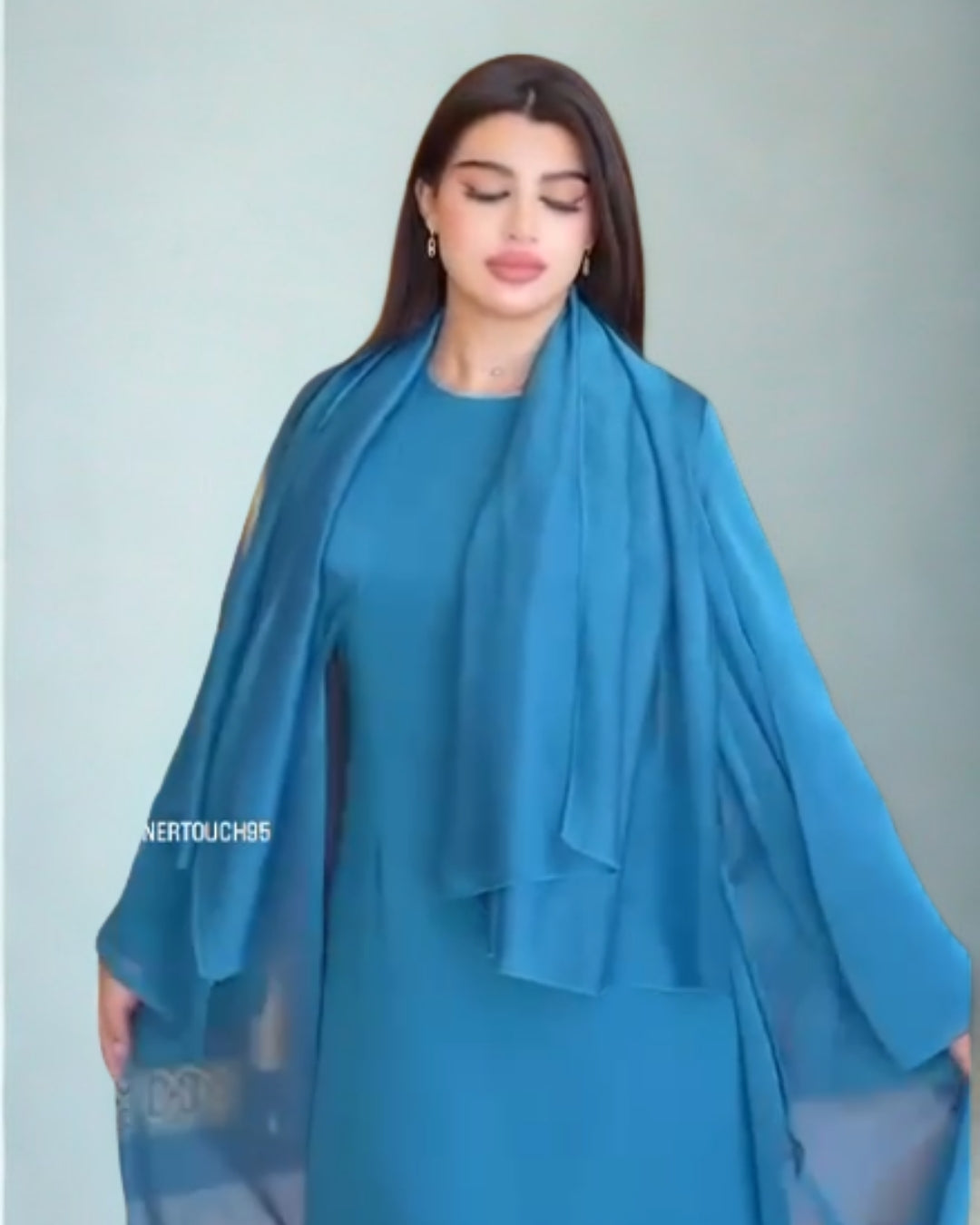 Woman wearing a blue dress with a matching scarf against a light gray background