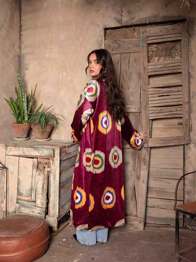 Woman wearing a long, patterned dress standing in a rustic room with wooden walls and furniture.