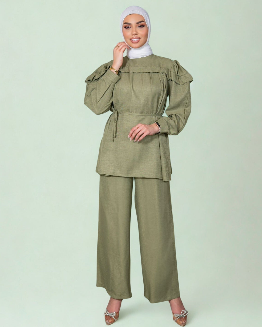 Woman wearing a green outfit with a matching hijab on a light green background