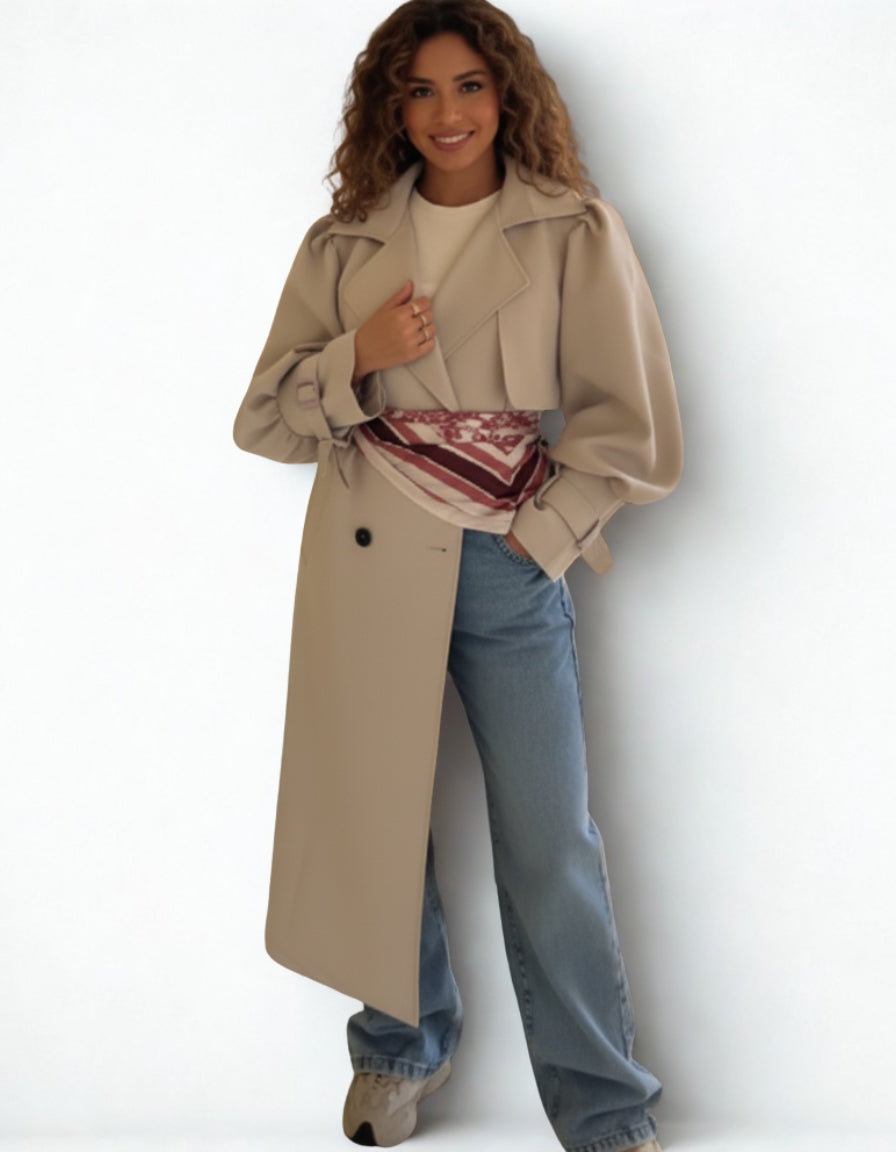 Woman wearing a beige trench coat and blue jeans against a white background