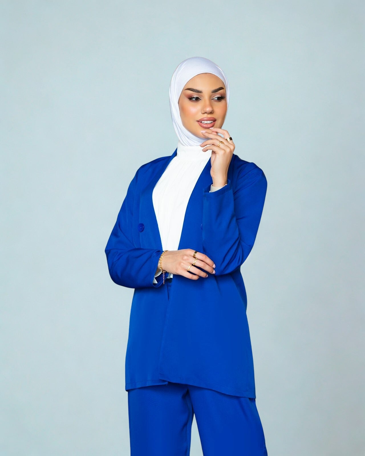 Woman wearing a blue outfit with a white hijab on a light gray background