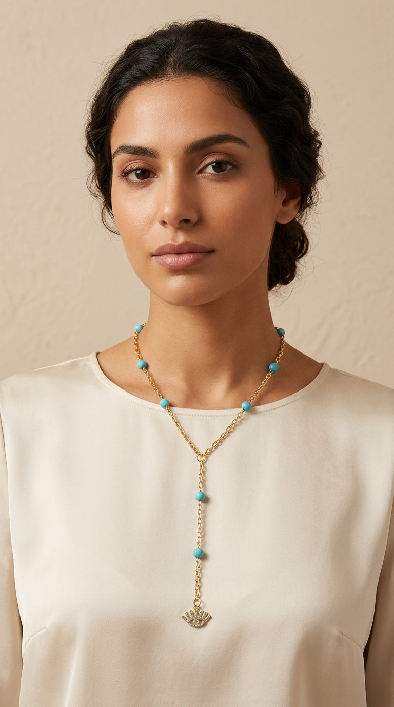 Woman wearing a necklace with turquoise beads and a gold pendant against a beige background