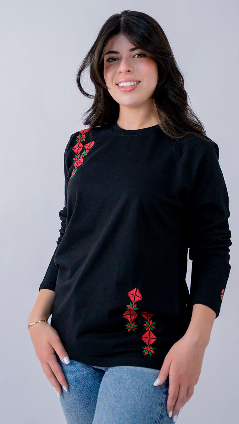 Woman wearing a black sweater with red floral embroidery on a plain background