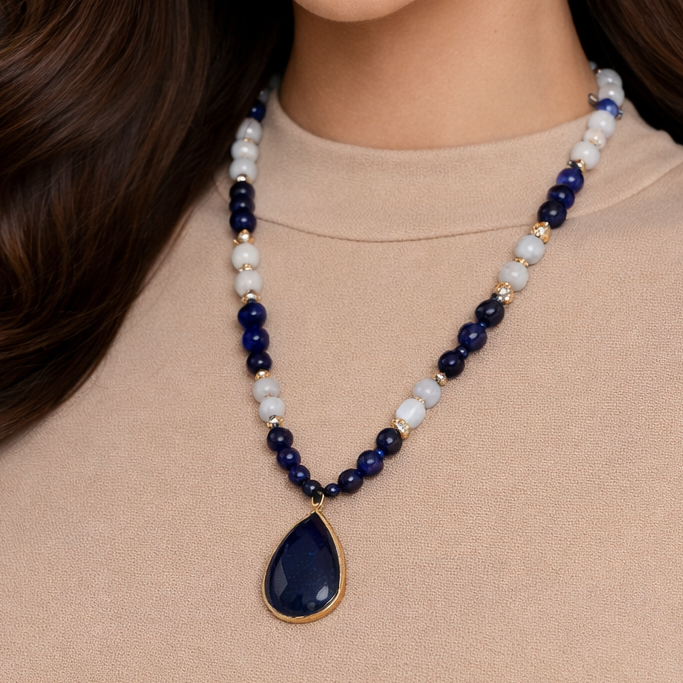 Woman wearing a blue beaded necklace with a large teardrop pendant on a plain background