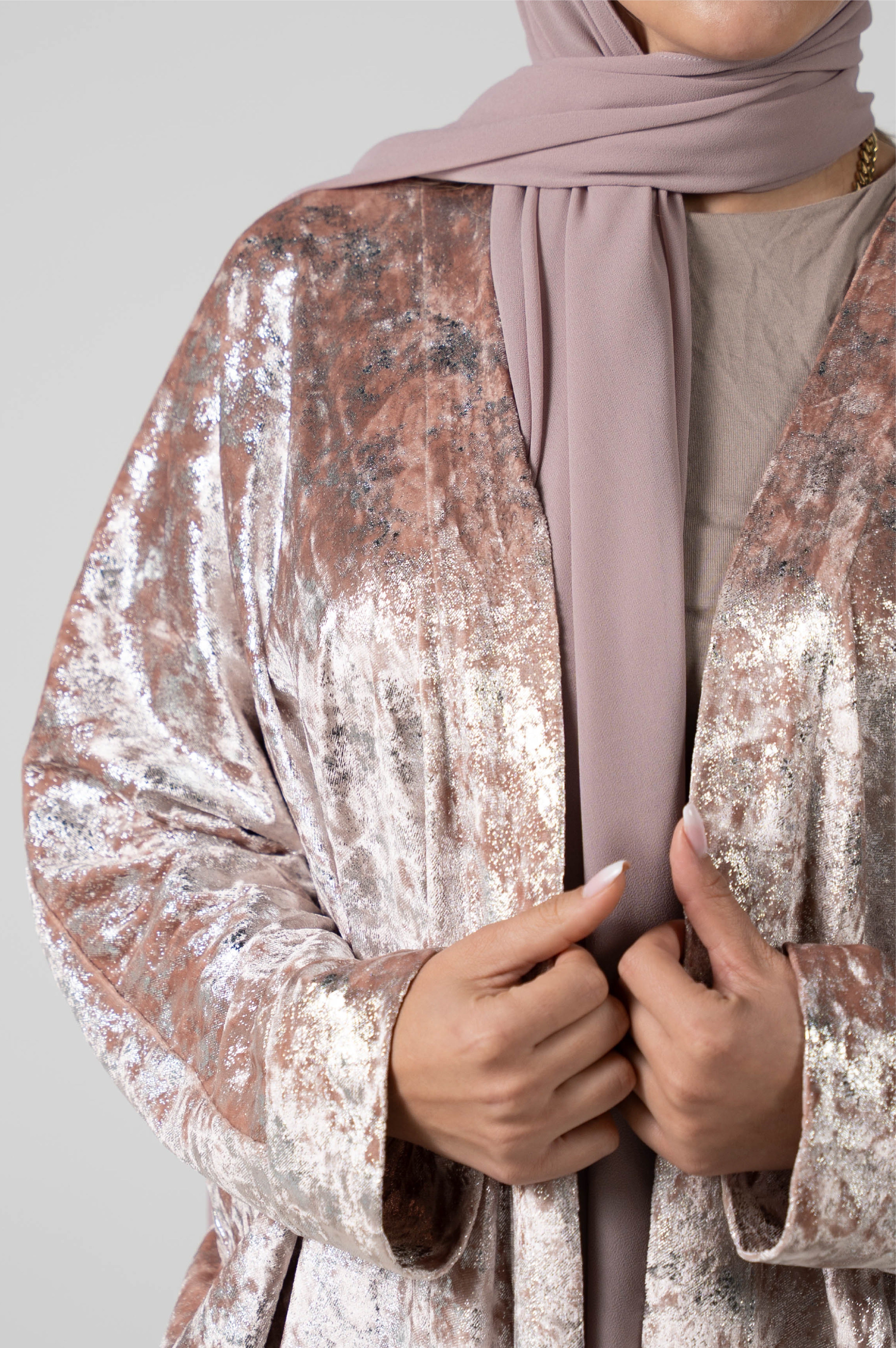 Person wearing a sparkling cardigan and a pink hijab on a plain background