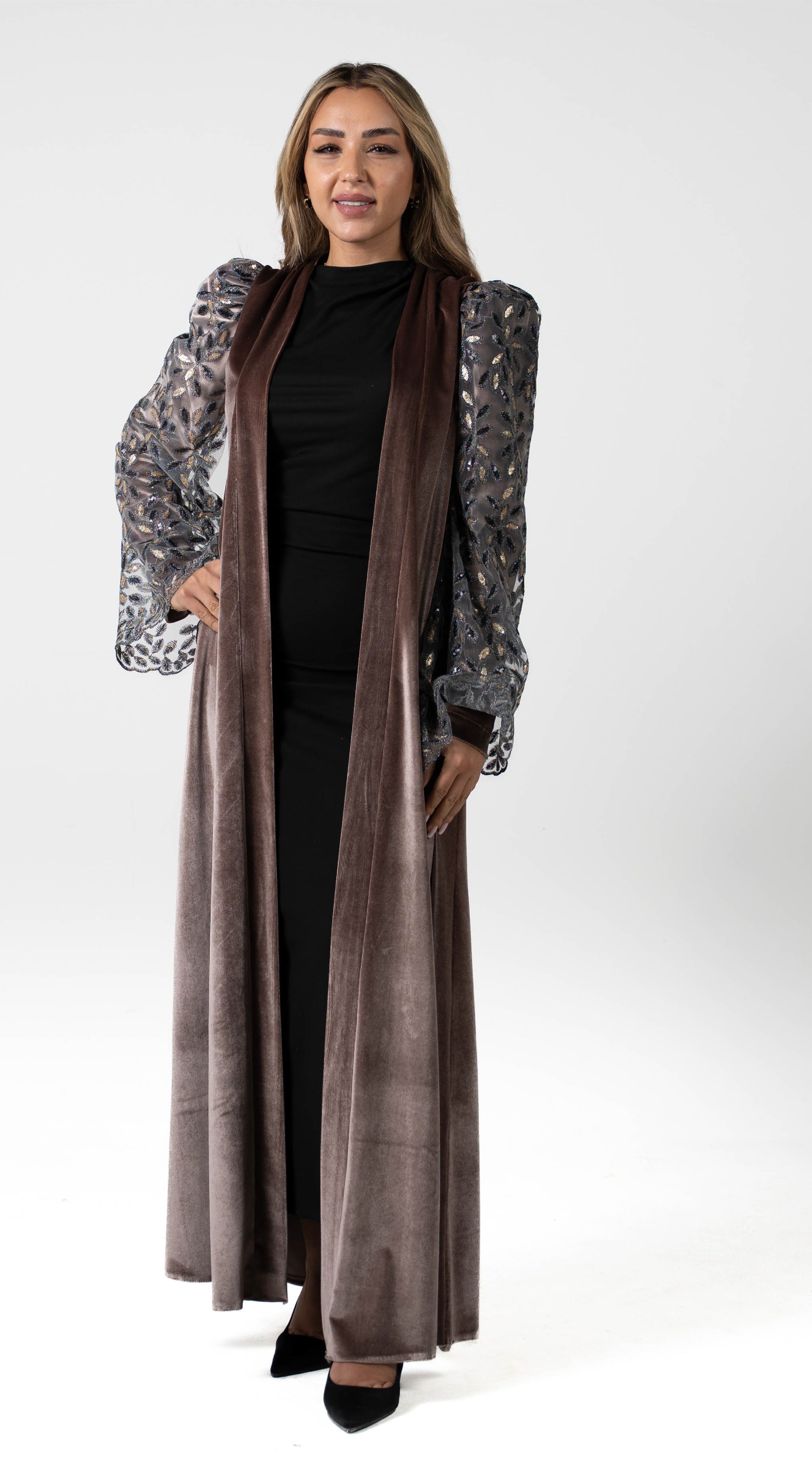 Woman wearing a long, patterned coat over a black dress on a white background