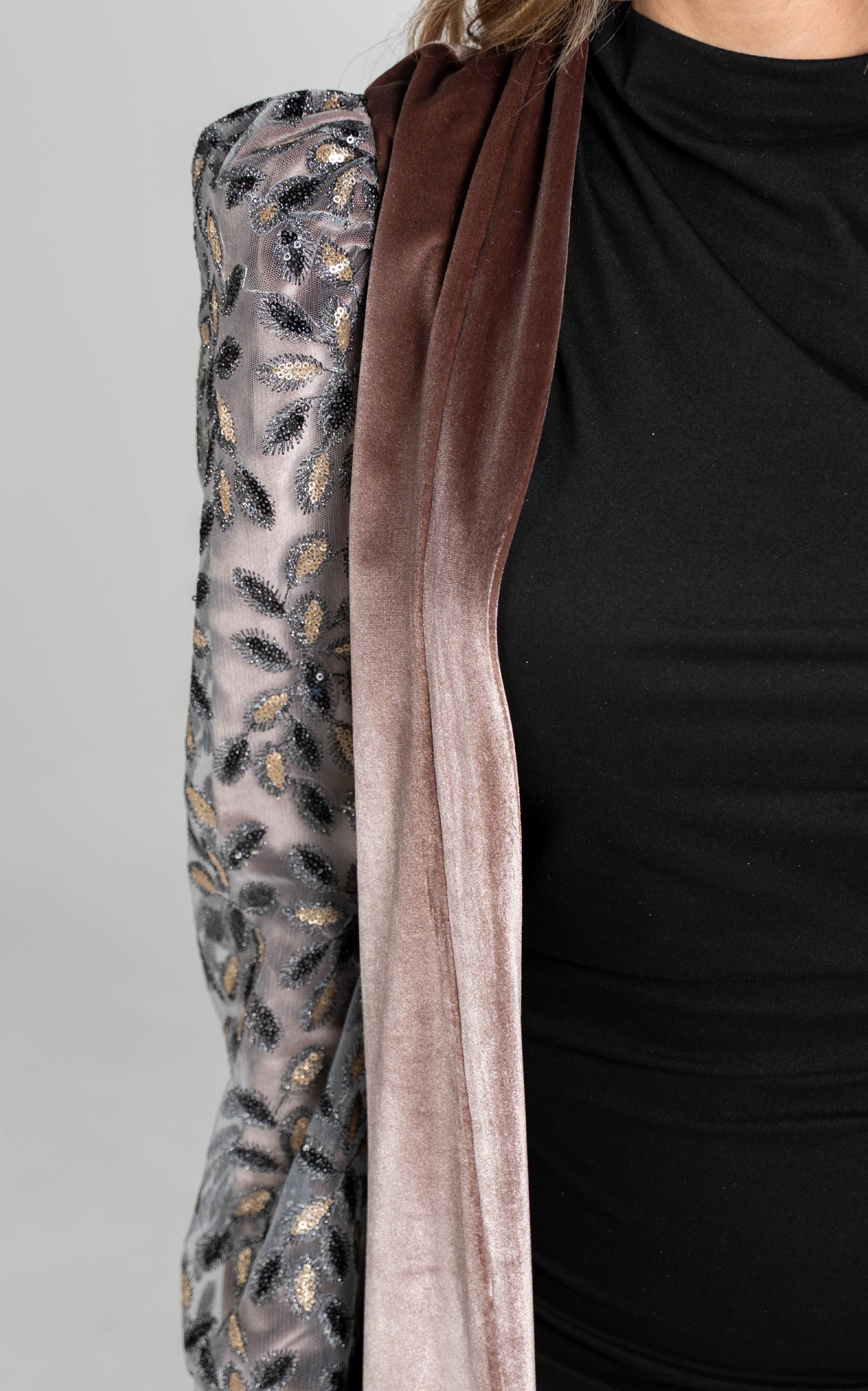 Close-up of a black garment with a brown ribbon and patterned fabric on a gray background