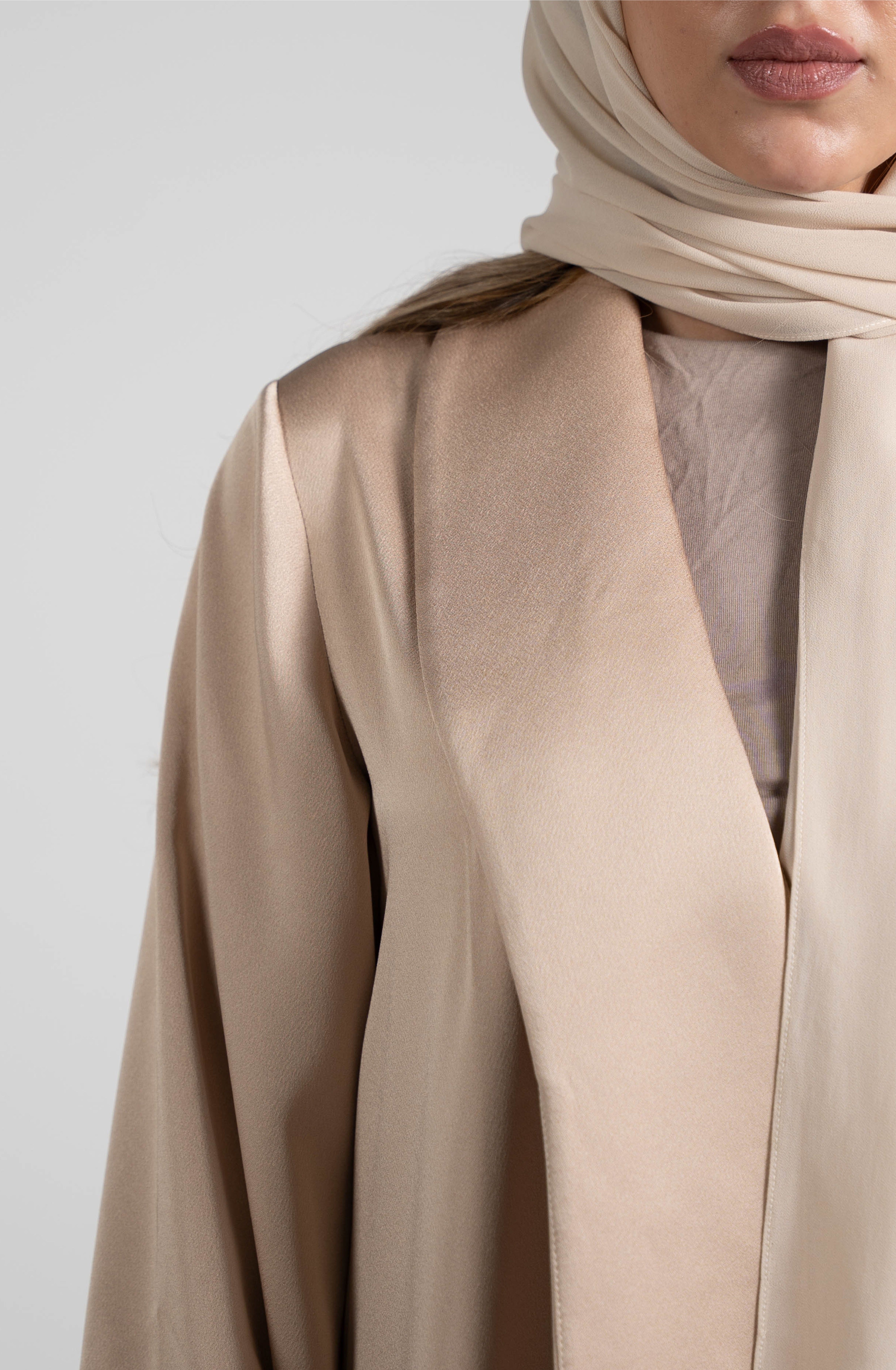 Person wearing a beige hijab and abaya against a white background