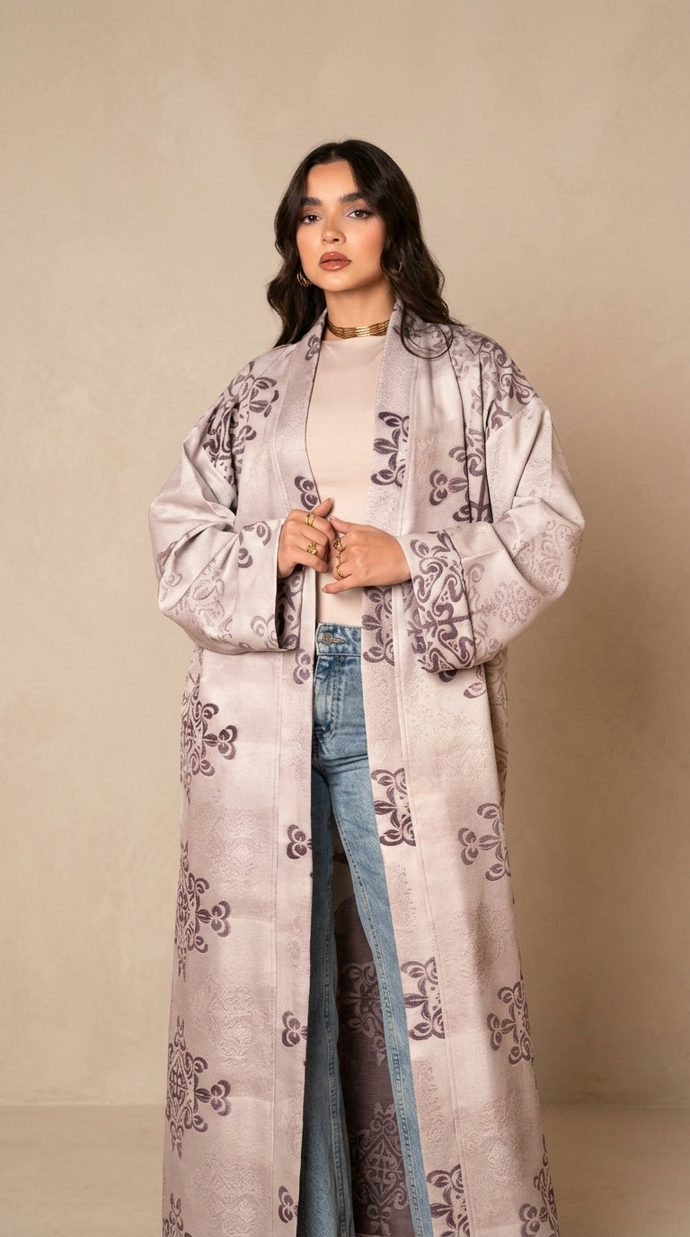 Woman wearing a long, patterned coat over a white top and blue jeans on a beige background