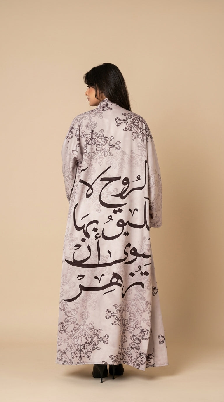 Woman wearing a long, light-colored coat with Arabic calligraphy on a beige background