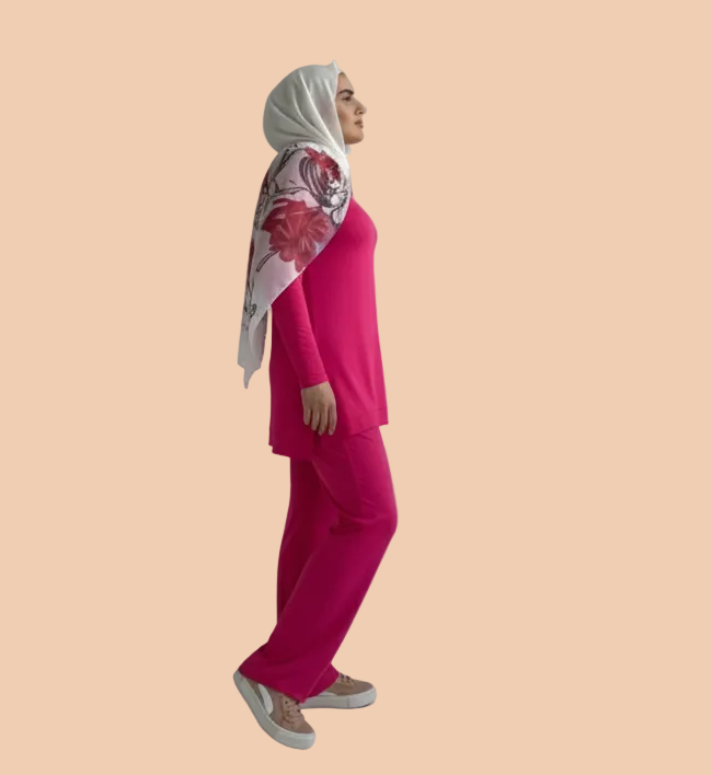 Person wearing a bright pink outfit with a patterned headscarf on a plain background