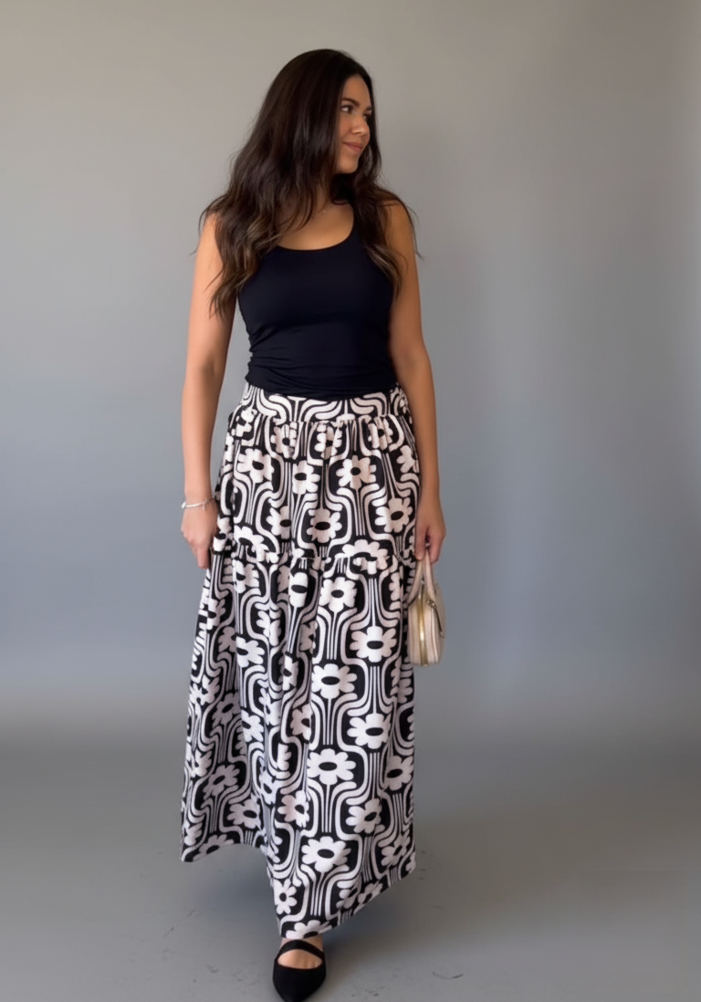 Woman wearing a black top and patterned skirt against a plain background