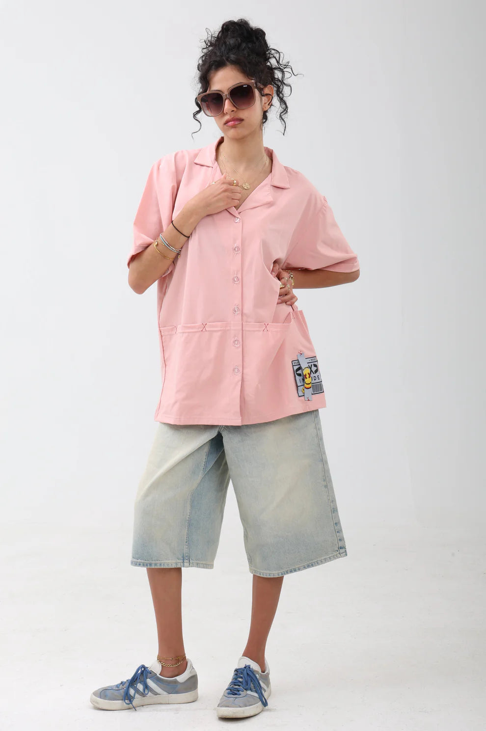 Person wearing a pink shirt with patches and light blue shorts on a white background