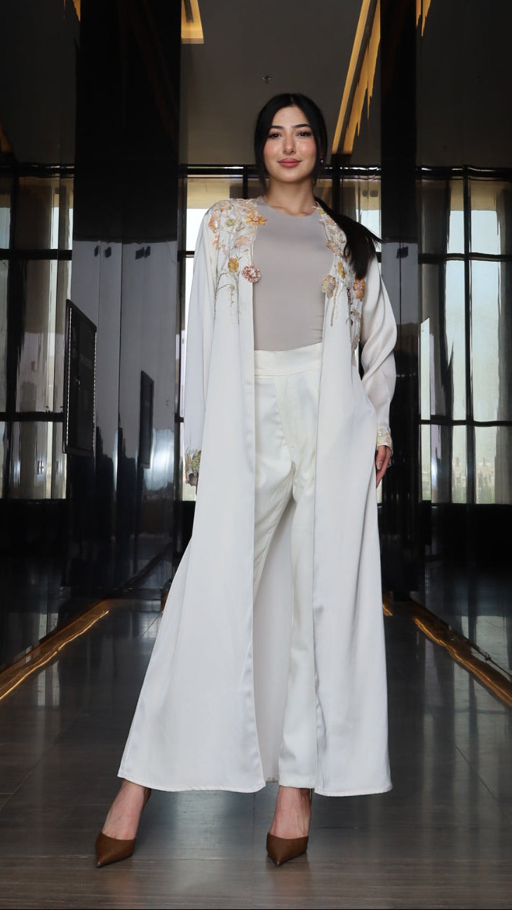 A woman wearing a white traditional Chinese outfit with gold embroidery, standing in a dark hallway with reflective glass panels.