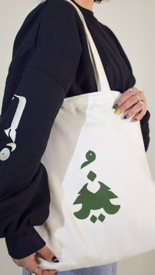 Person holding a white tote bag with a green design against a plain background