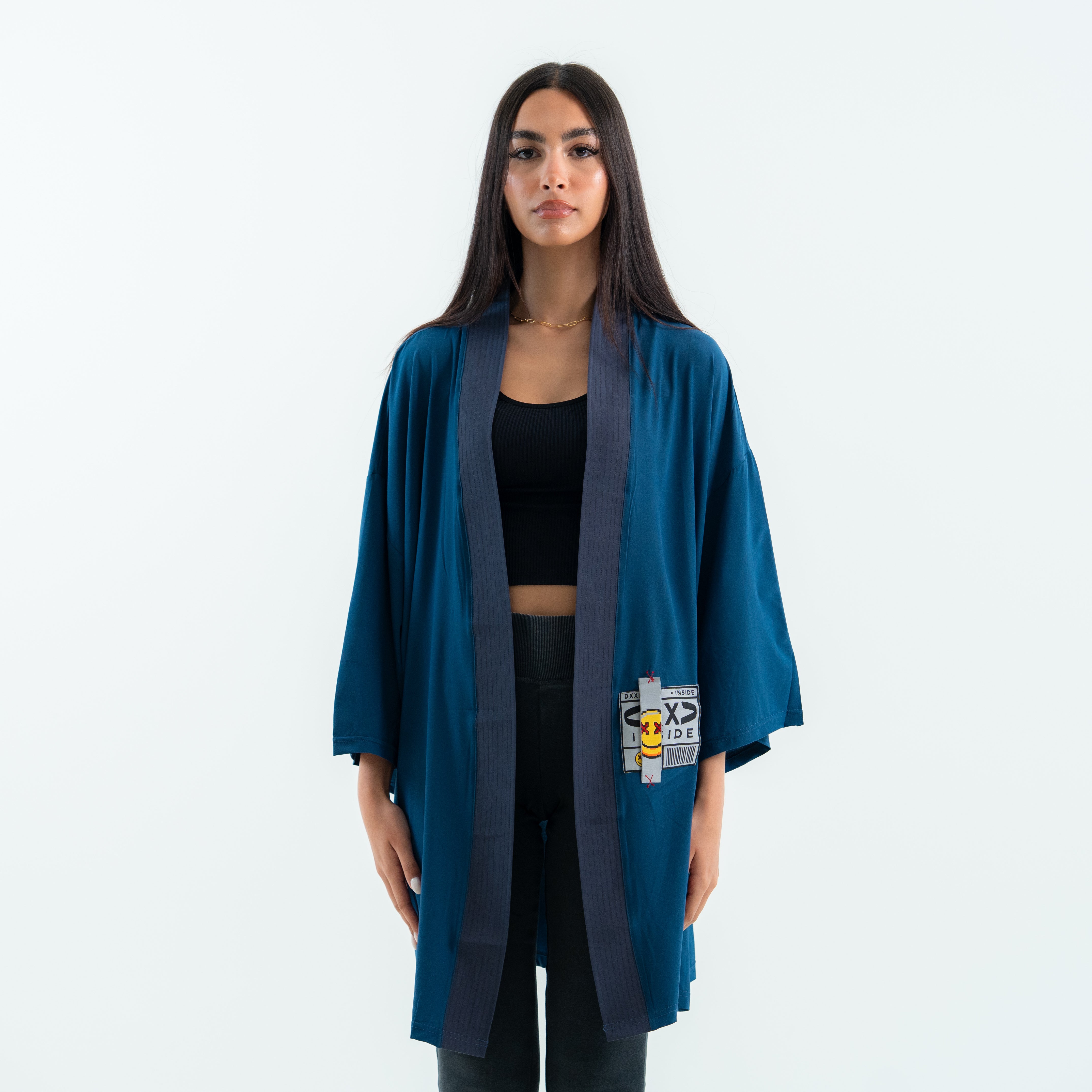 Woman wearing a teal kimono-style jacket with a patch on a white background