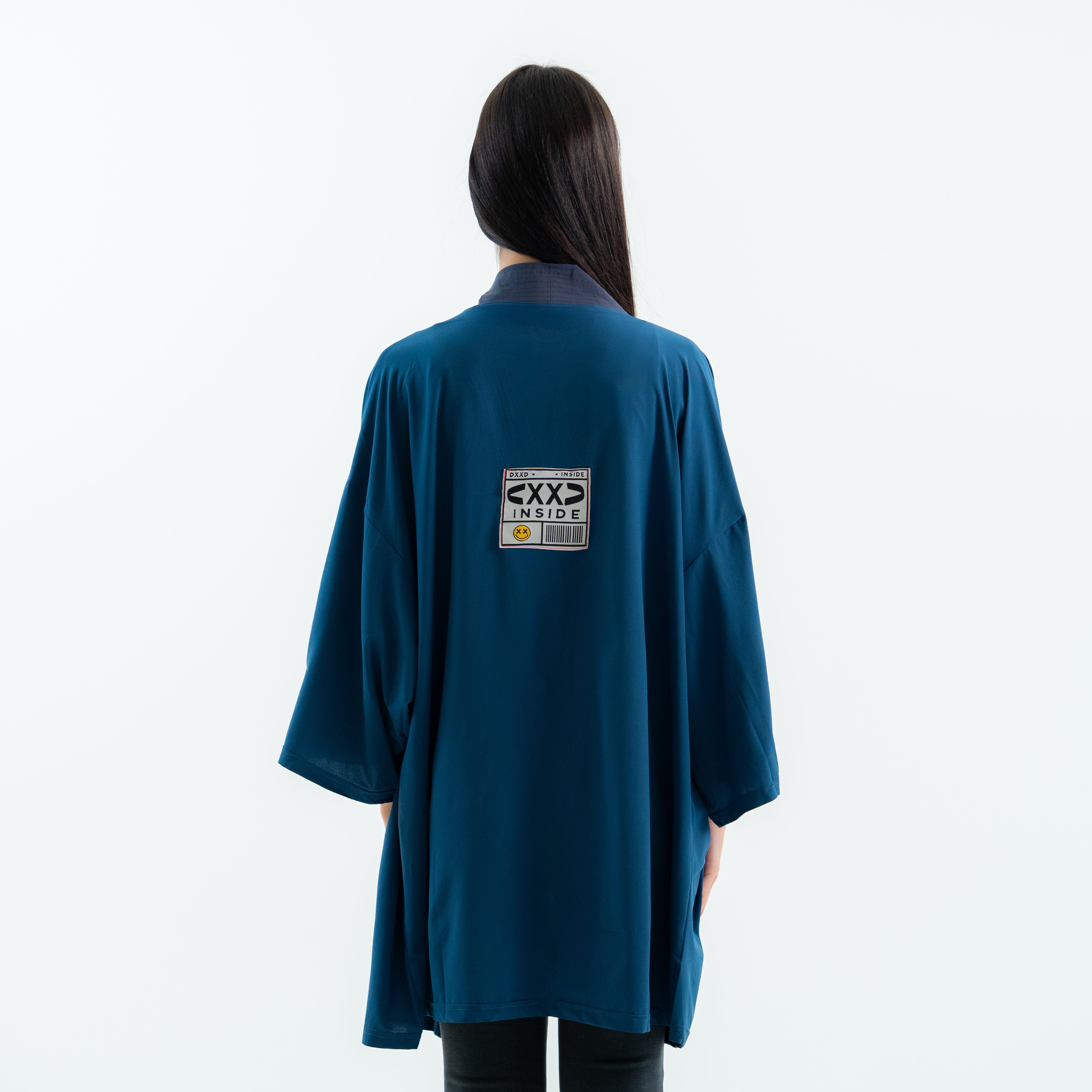 Person wearing a teal coat with a label on the back against a white background