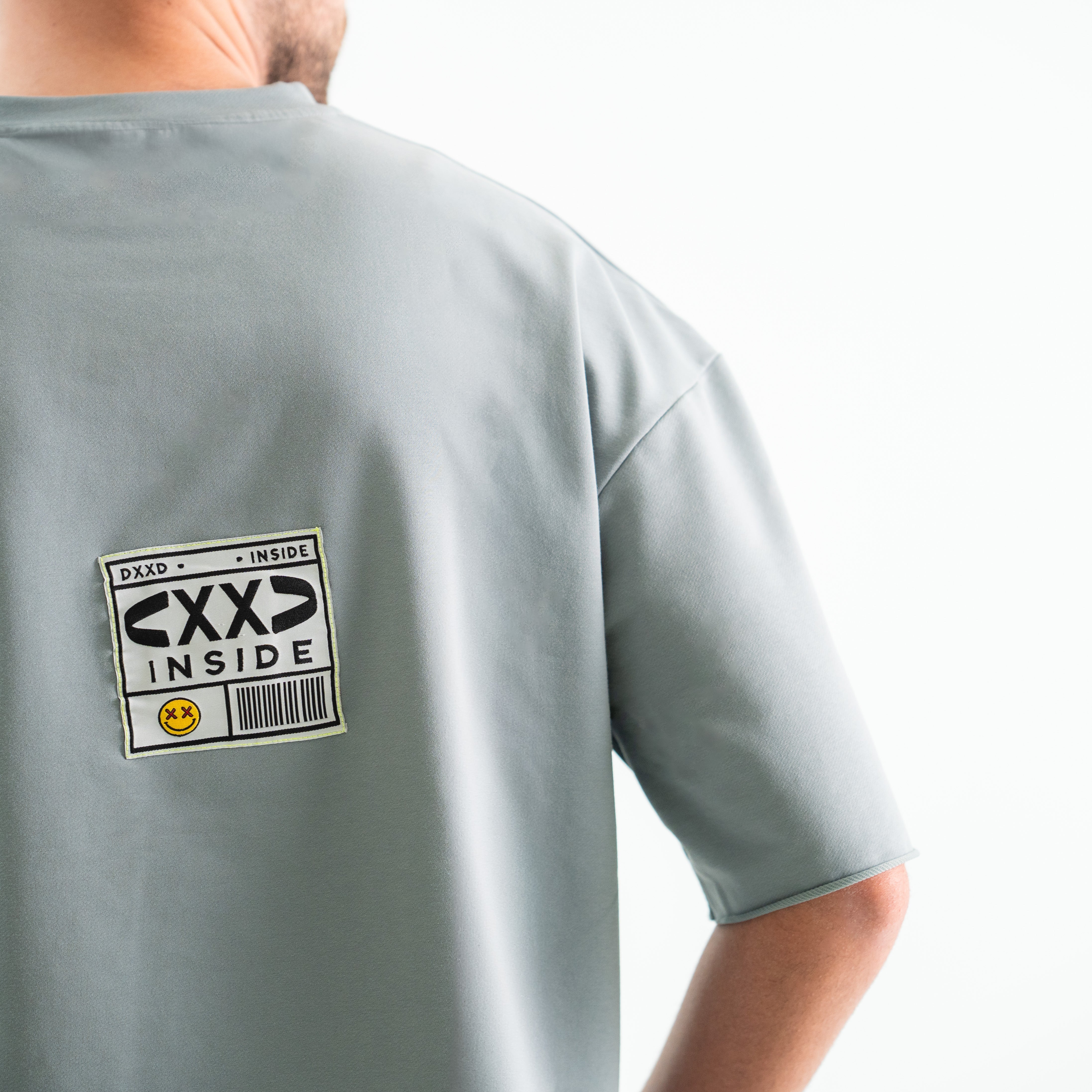 Gray t-shirt with 'CXXD INSIDE' label on the back against a white background