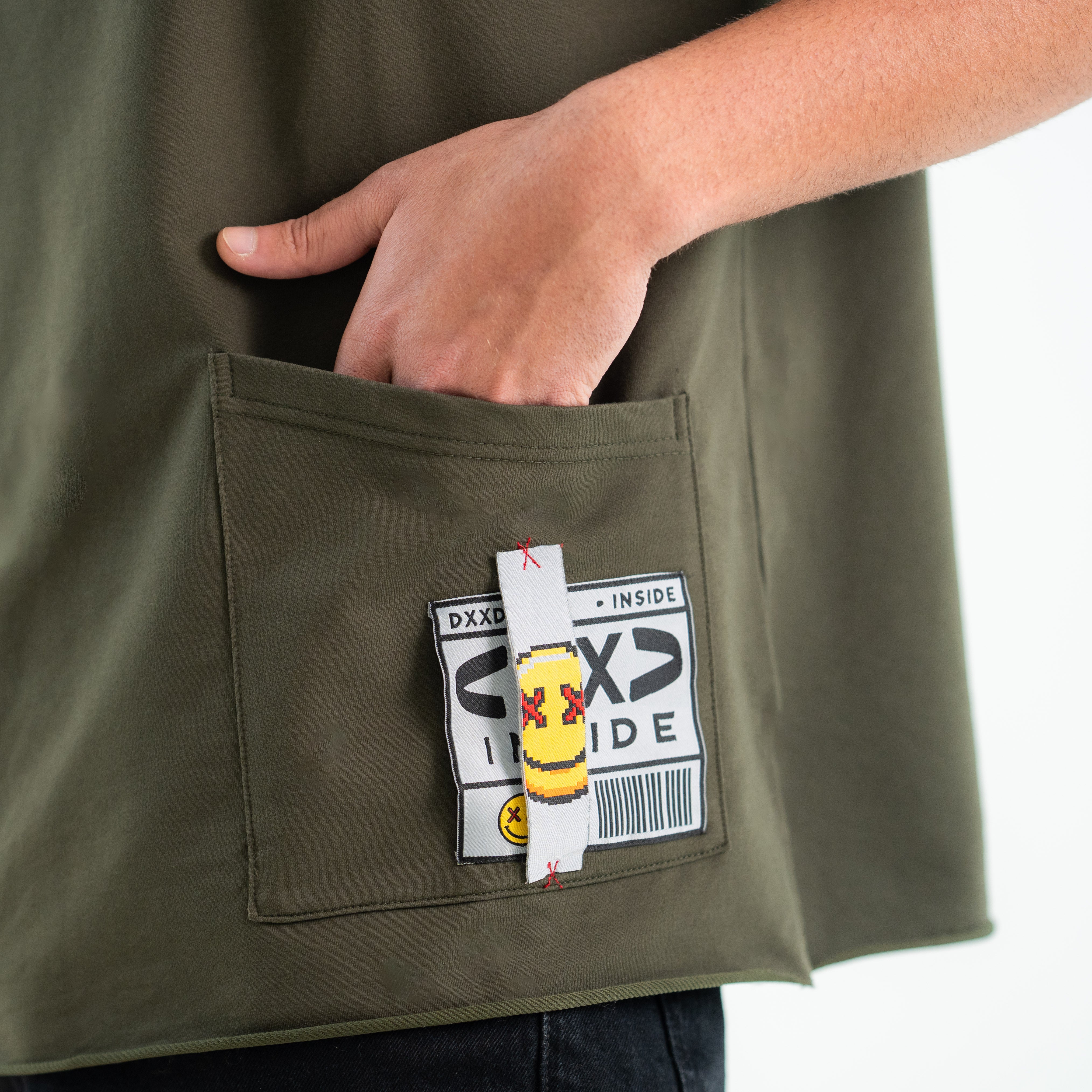 Person wearing a green jacket with a pocket featuring a label and small figure.