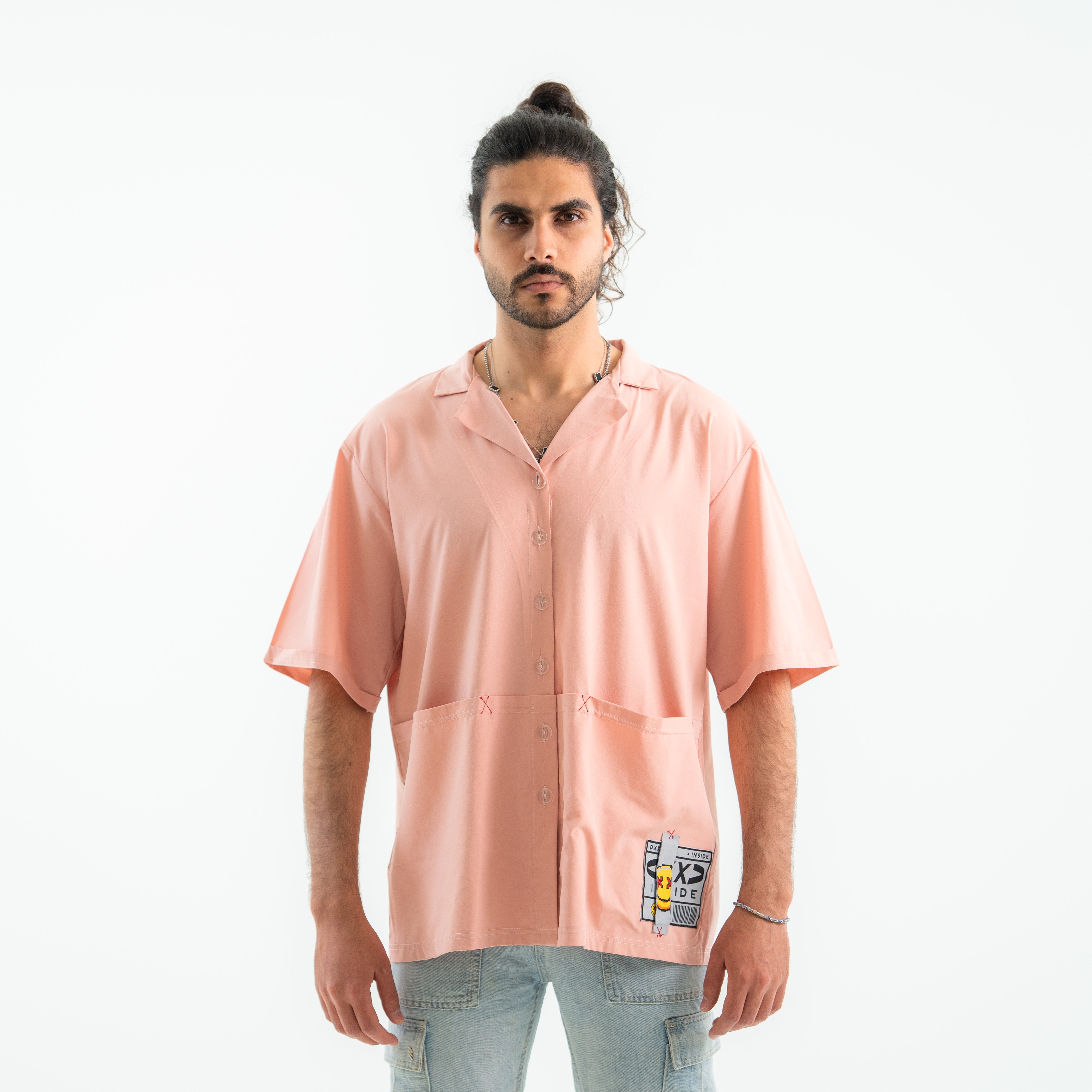 Man wearing a light pink button-up shirt with a patch on a white background