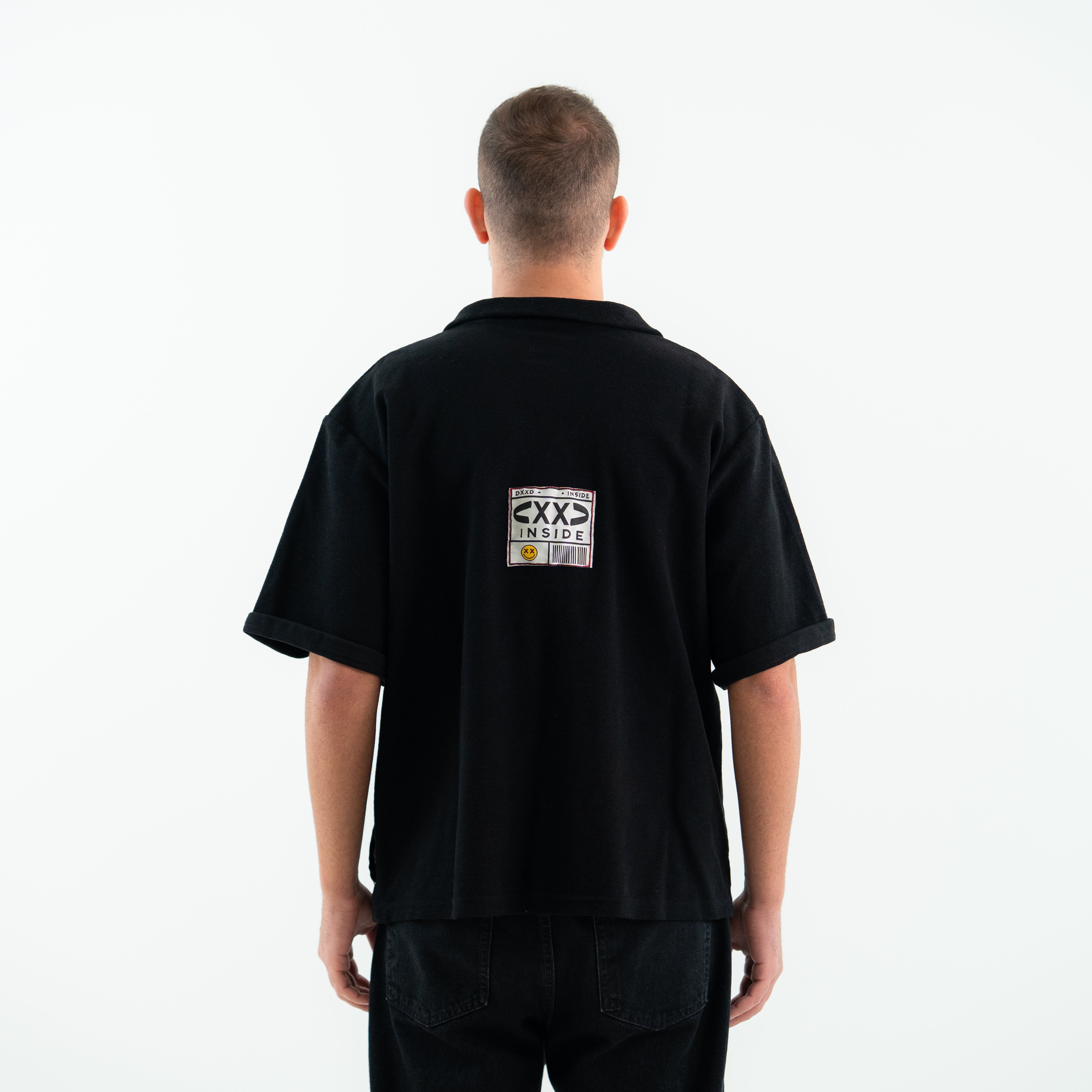 Person wearing a black polo shirt with a logo on the back against a white background