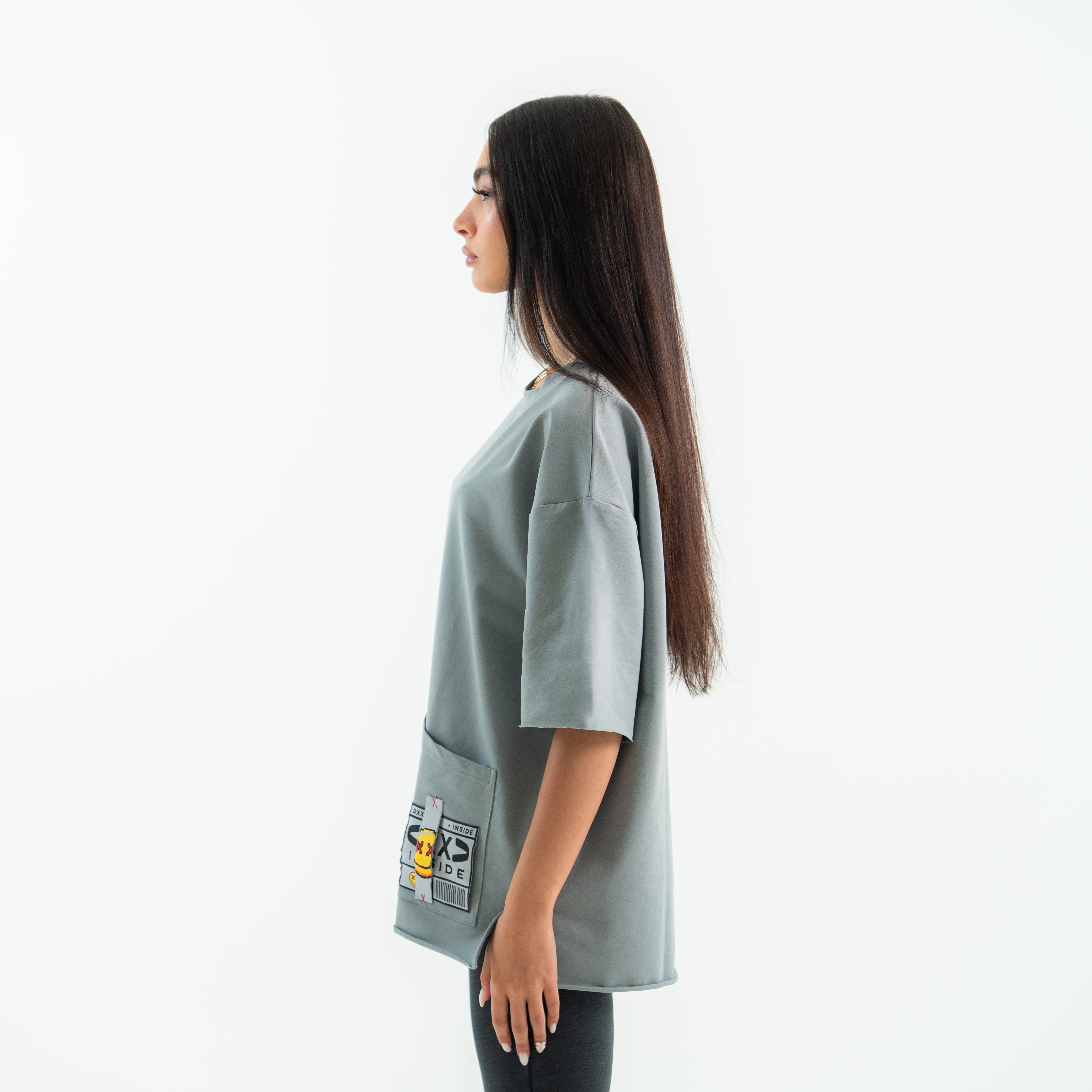 Woman wearing a light gray oversized shirt with patches on a white background