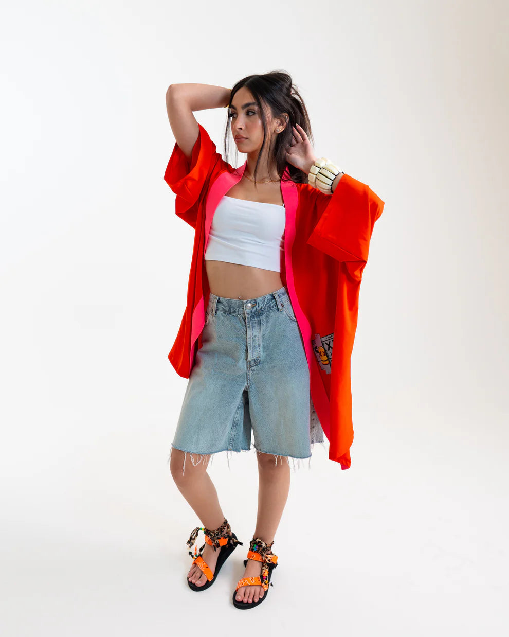 Woman wearing a bright orange kimono-style garment over a white top and denim skirt on a white background