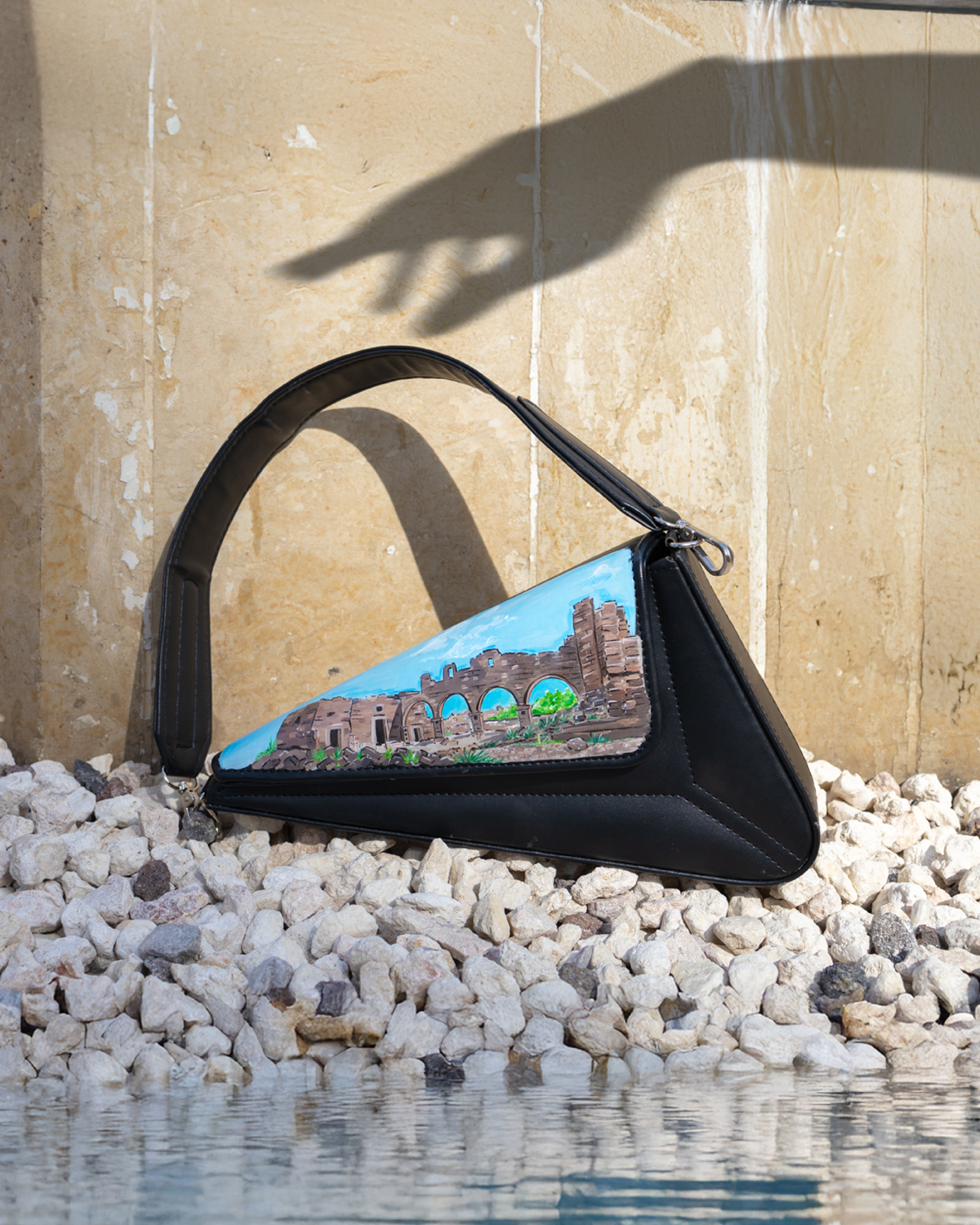 Black handbag with a scenic design on pebbles by a pool