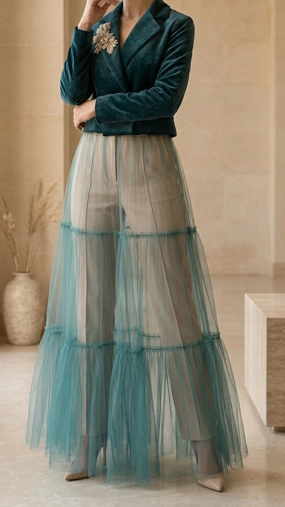 Woman in a teal velvet top and layered tulle skirt standing in a beige room.