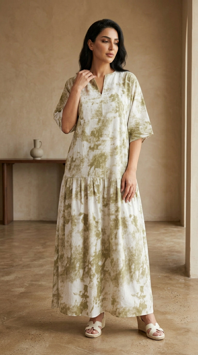 Woman wearing a long, light-colored dress with a subtle pattern in a warm-toned room.