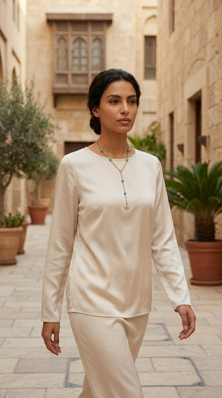 Woman in a white outfit standing in an outdoor setting with stone buildings and plants.