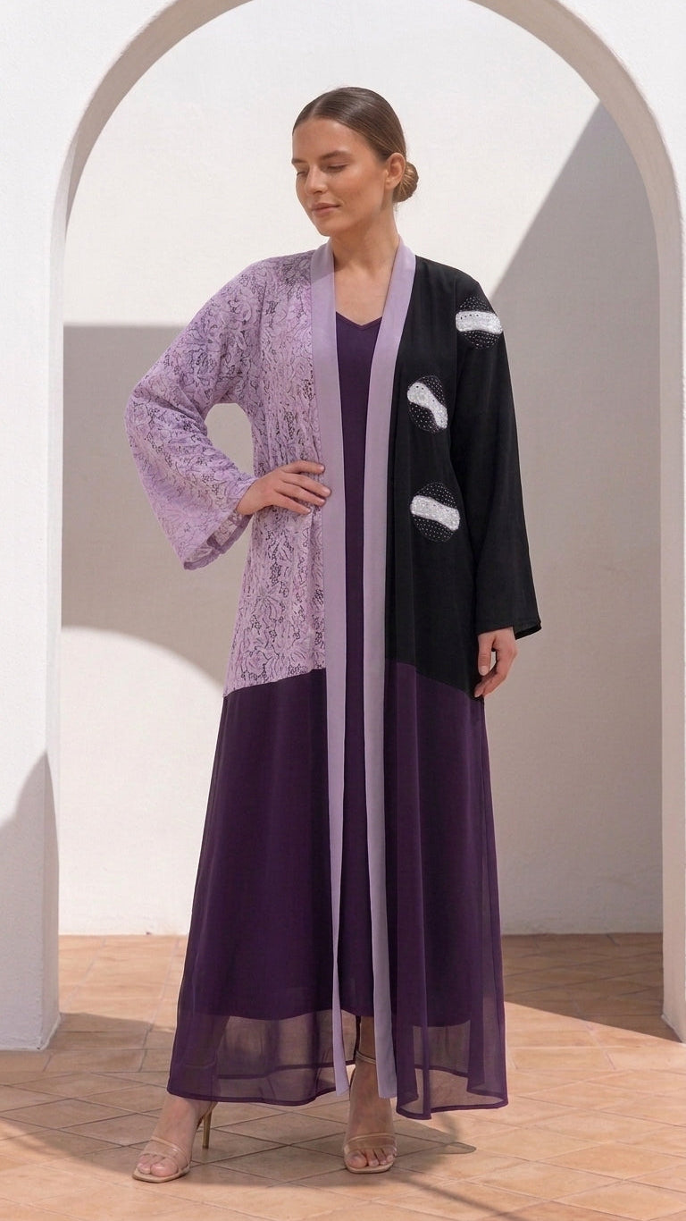 A woman models a three-piece modest outfit consisting of a lavender embroidered long-sleeve abaya, a black open-front jacket with white accents, and a matching dark purple maxi skirt, set against a white arched wall.