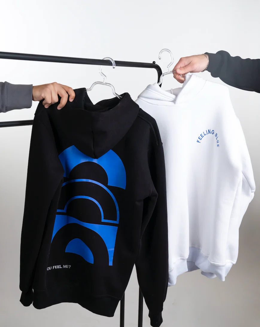 Black hoodie with blue graphic and white sweatshirt on hangers against a white background