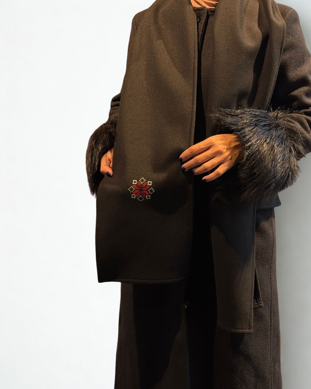 Brown coat with fur trim and a decorative emblem on a white background