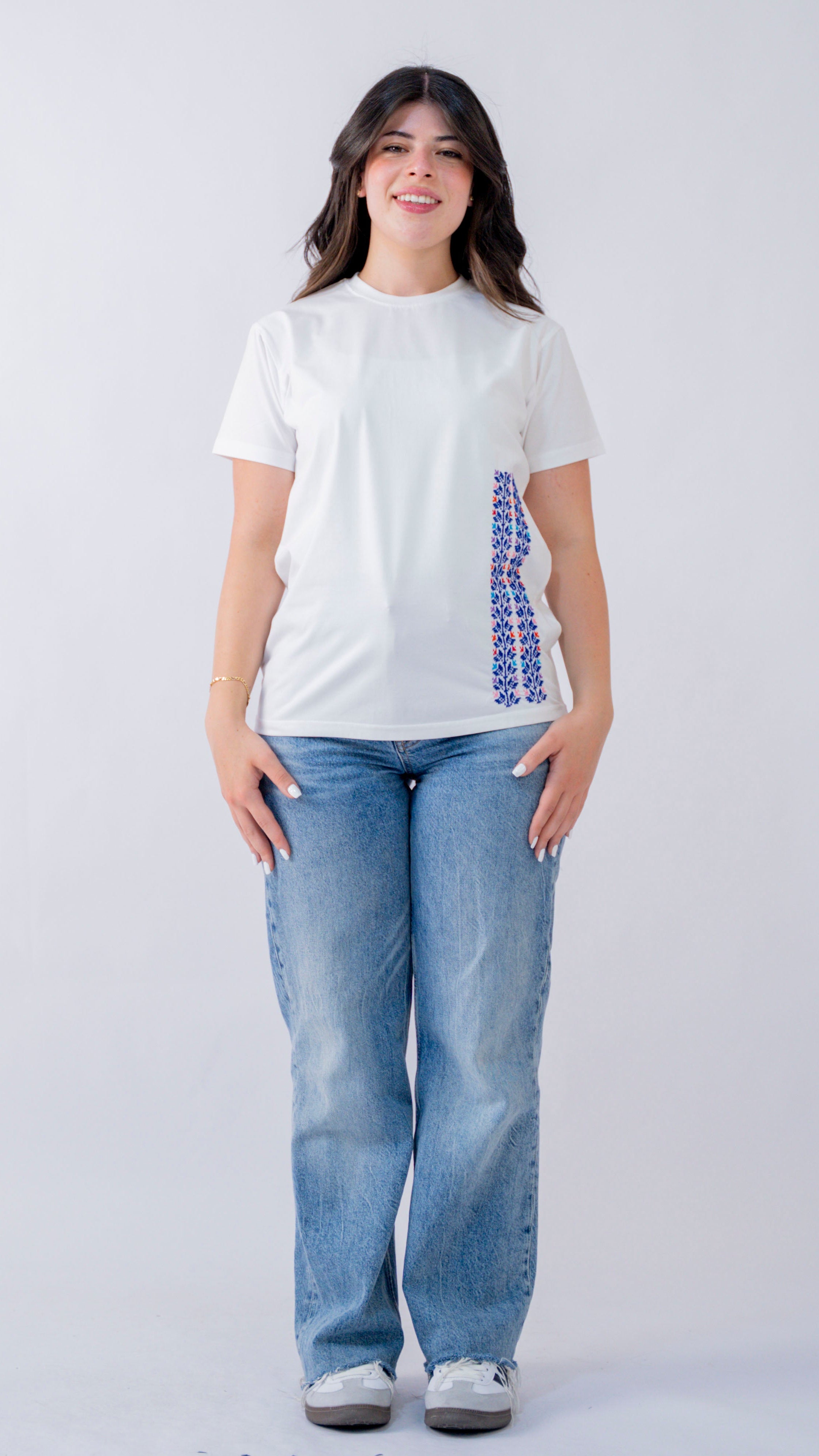 Person wearing a white t-shirt with a graphic design and blue jeans on a plain background