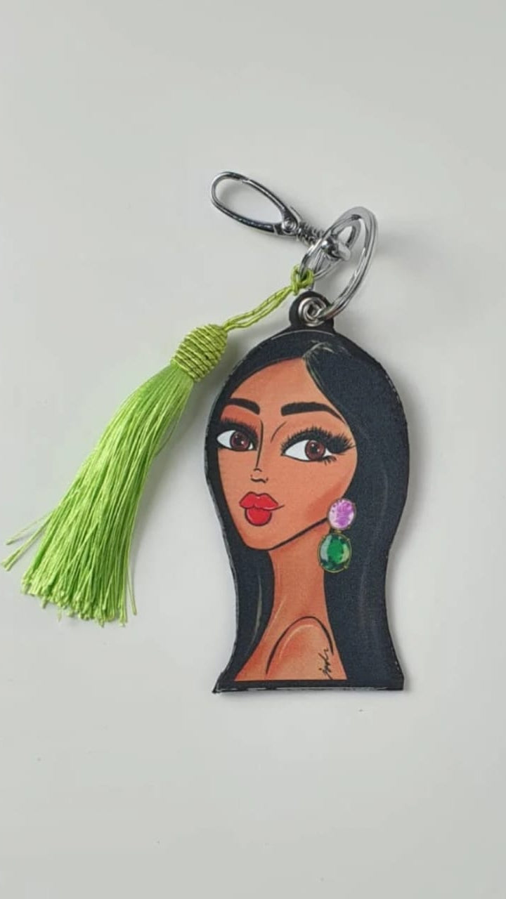Keychain with a face design and green tassel on a light gray background