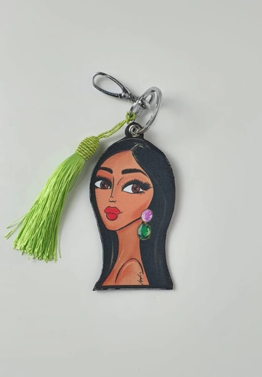 Keychain with a face design and green tassel on a light gray background