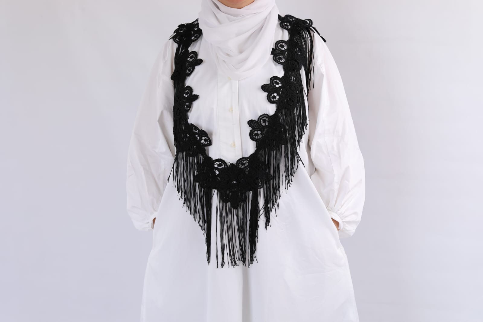 White outfit with a black fringed accessory on a plain background