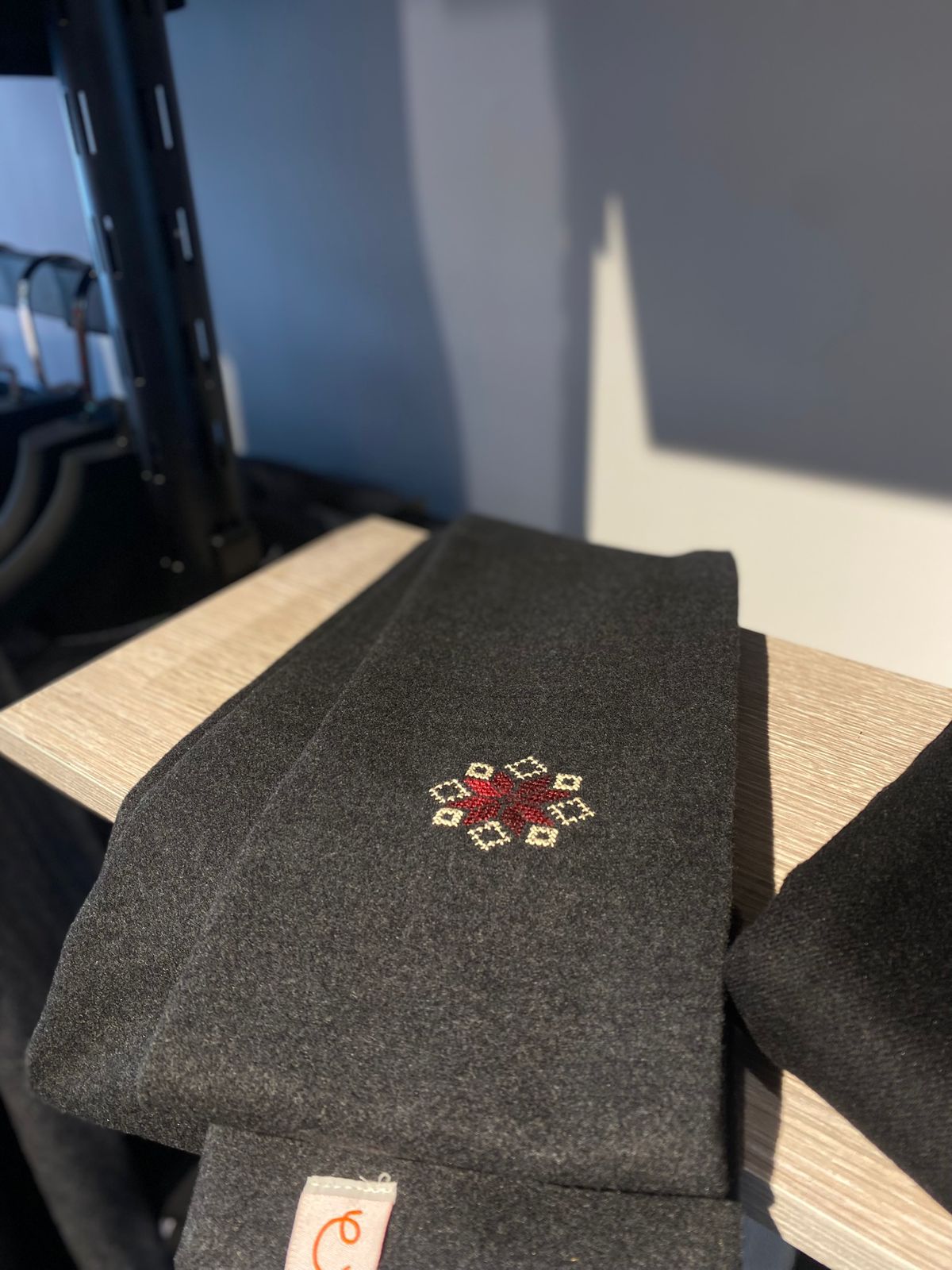Dark gray scarf with a red and white embroidered design on a wooden surface.