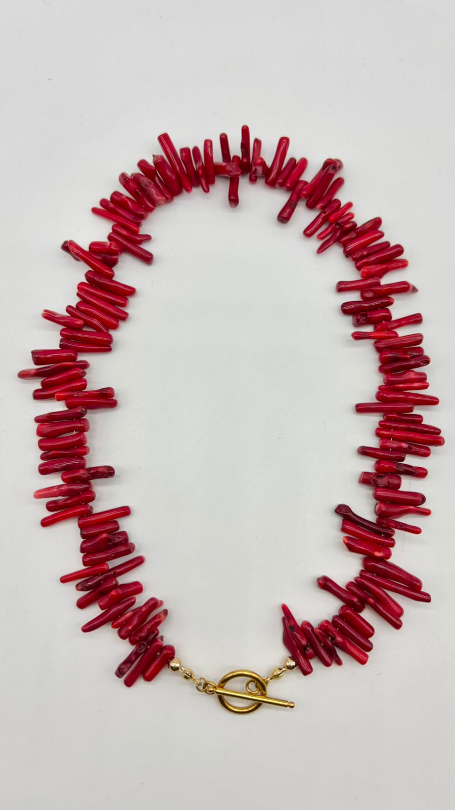 A red coral-style chunky necklace with a gold toggle clasp, laid flat on a light gray background.