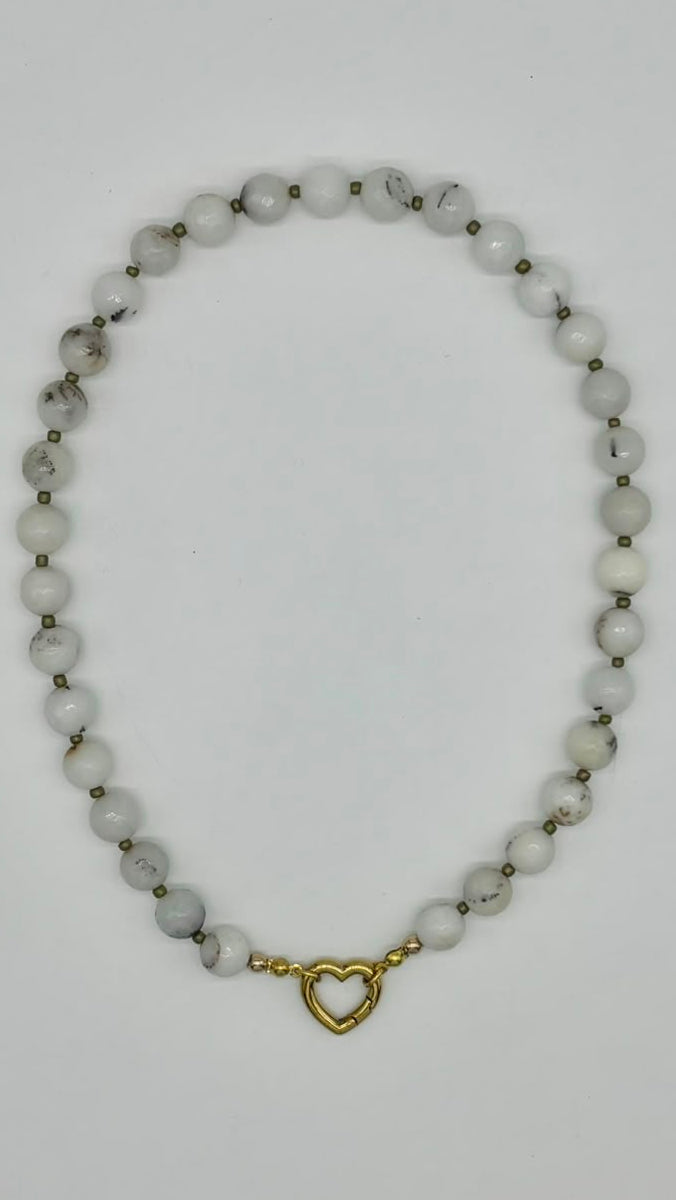 A beaded necklace made of small white beads with subtle gray marbling, separated by tiny metallic spacer beads, and finished with a small gold heart-shaped clasp, shown on a plain white background.