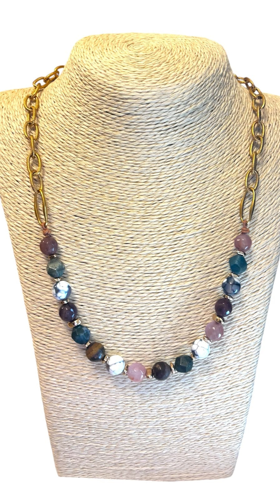 A gold-tone chain necklace with faceted multicolor beads, displayed on a beige textured mannequin bust against a white background.