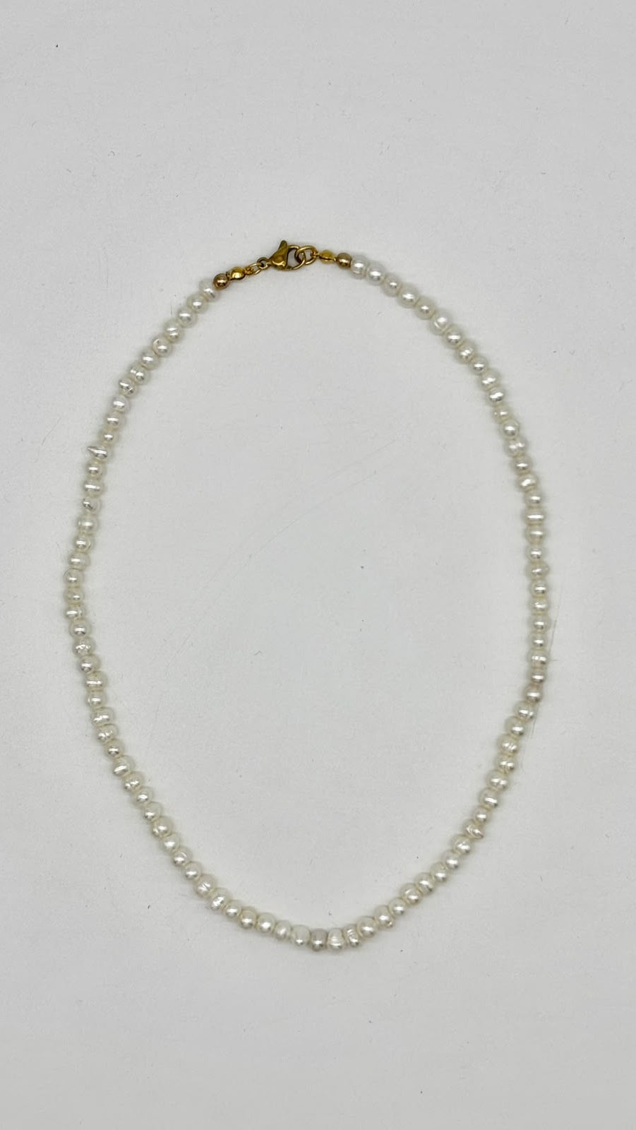 A single-strand pearl necklace with a gold clasp, laid flat on a light gray background.